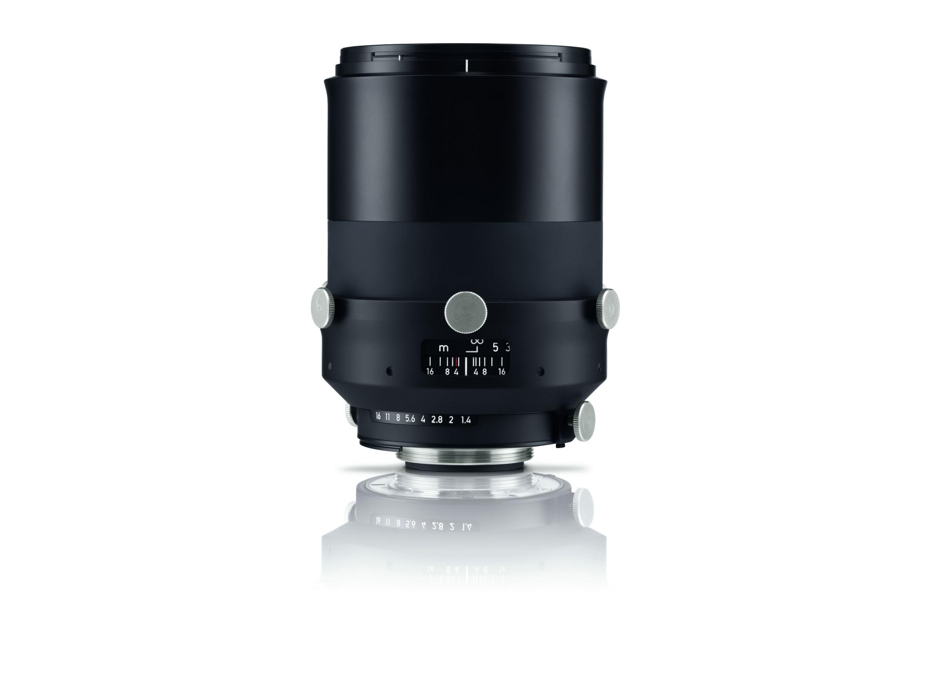 Black ZEISS camera lens with focus and aperture markings, shown upright on a white reflective surface.