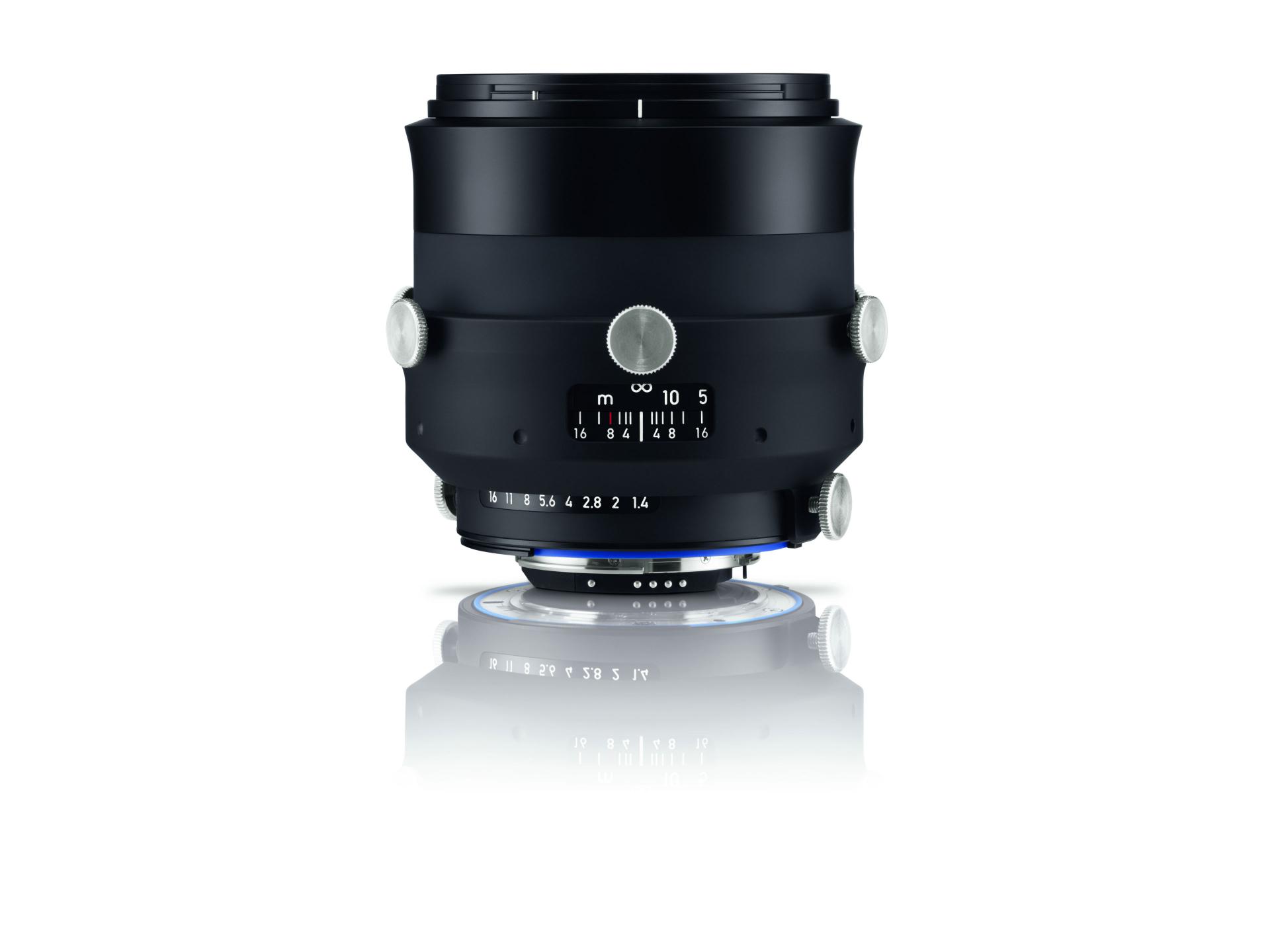 Black ZEISS camera lens with silver adjustment knobs and detailed focus markings, displayed upright on a reflective white surface.