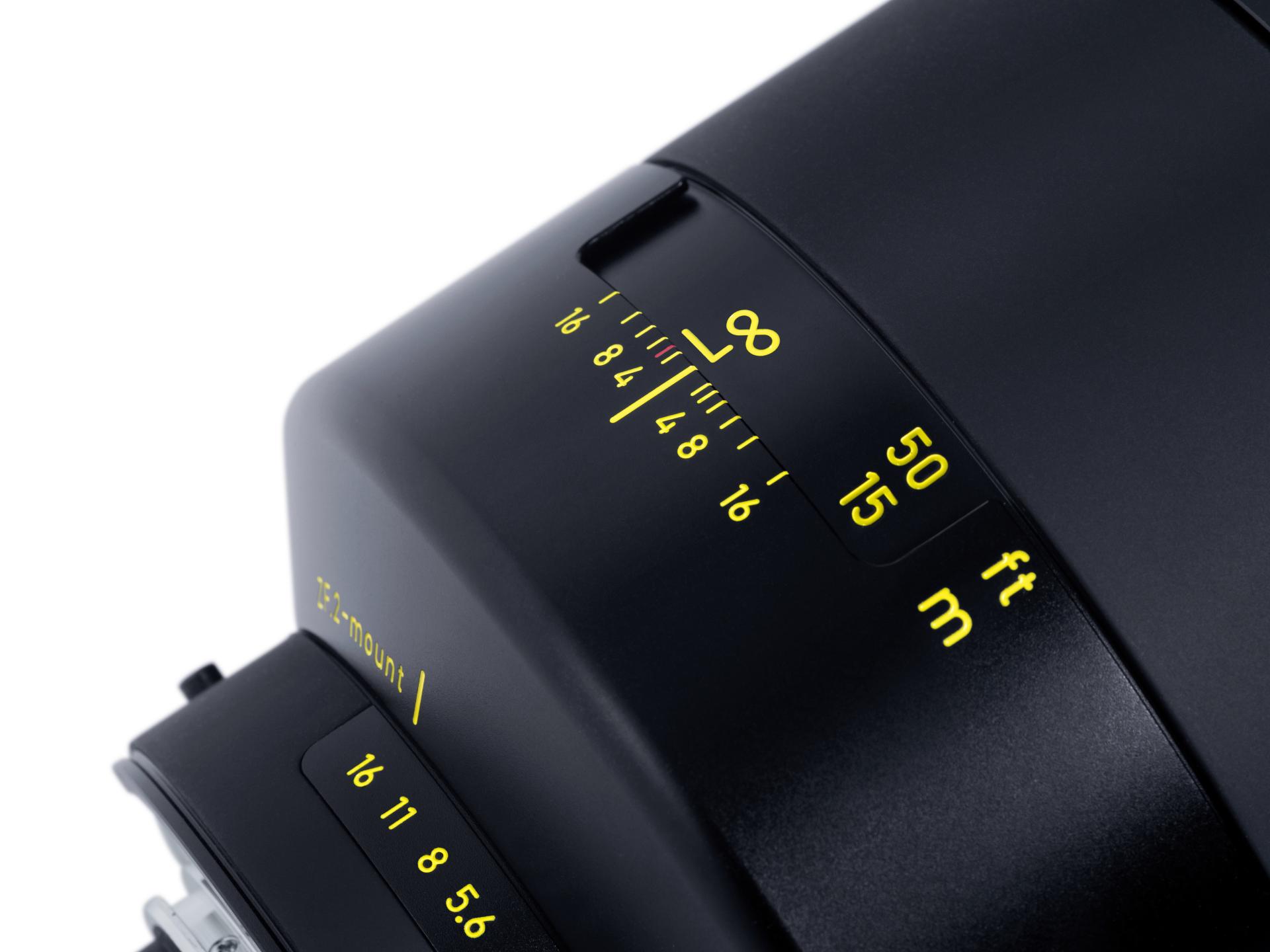 Close-up of a ZEISS camera lens showing distance and aperture markings in yellow on a black surface.