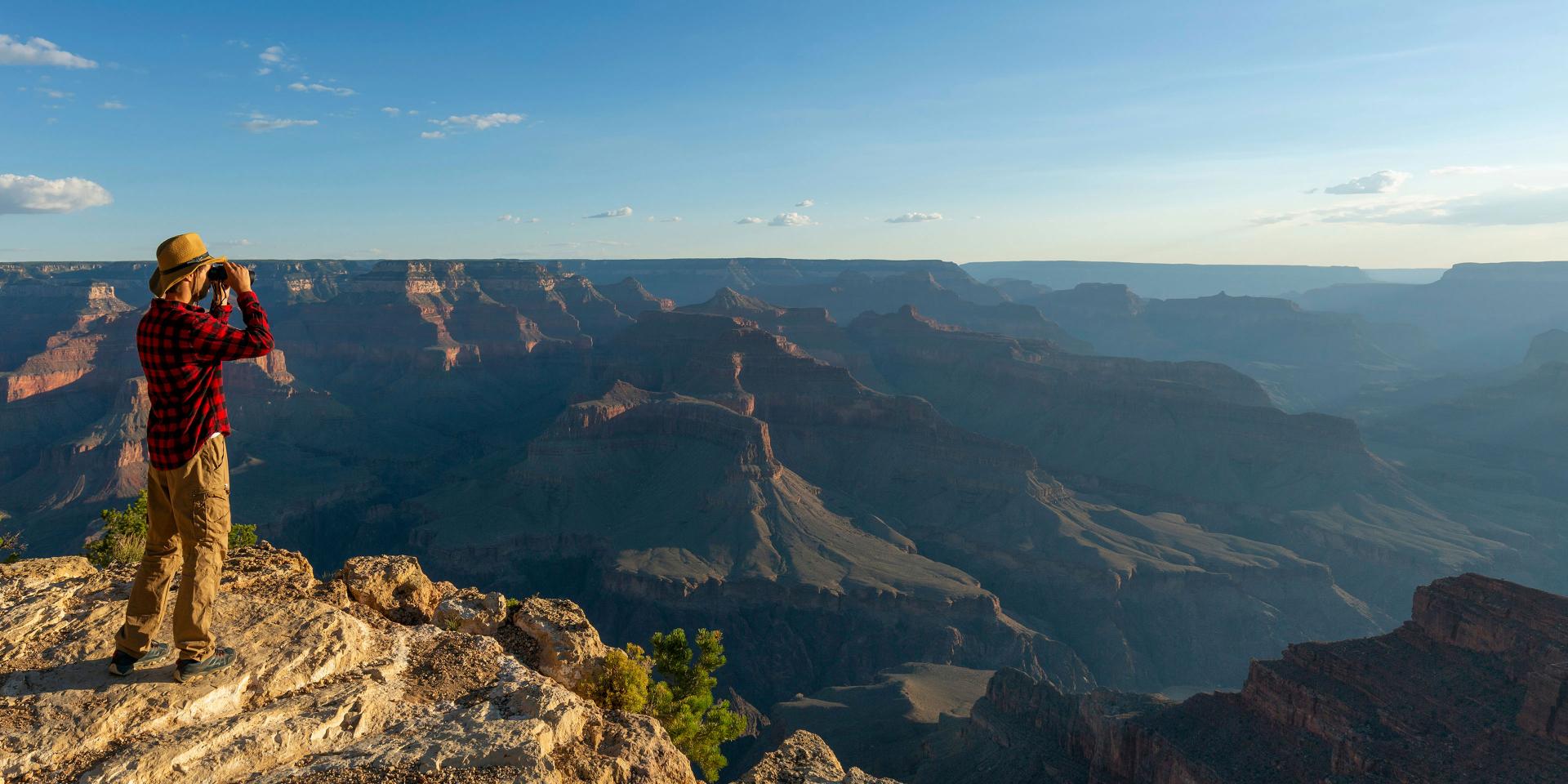 A person stands on the edge of a cliff overlooking the Grand Canyon while using ZEISS binoculars.