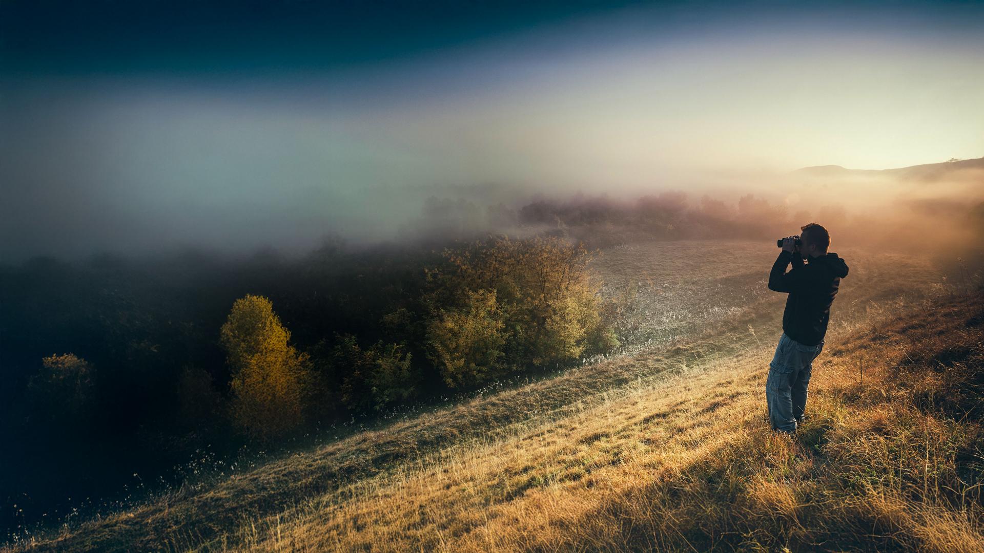 A person using ZEISS binoculars at sunrise to observe the misty landscape, capturing the clarity and precision of ZEISS optics in natural surroundings.
