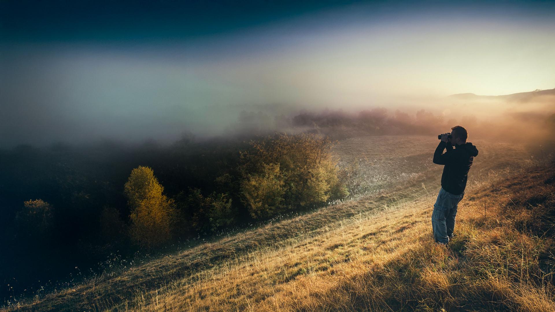A person using ZEISS binoculars at sunrise to observe the misty landscape, capturing the clarity and precision of ZEISS optics in natural surroundings.