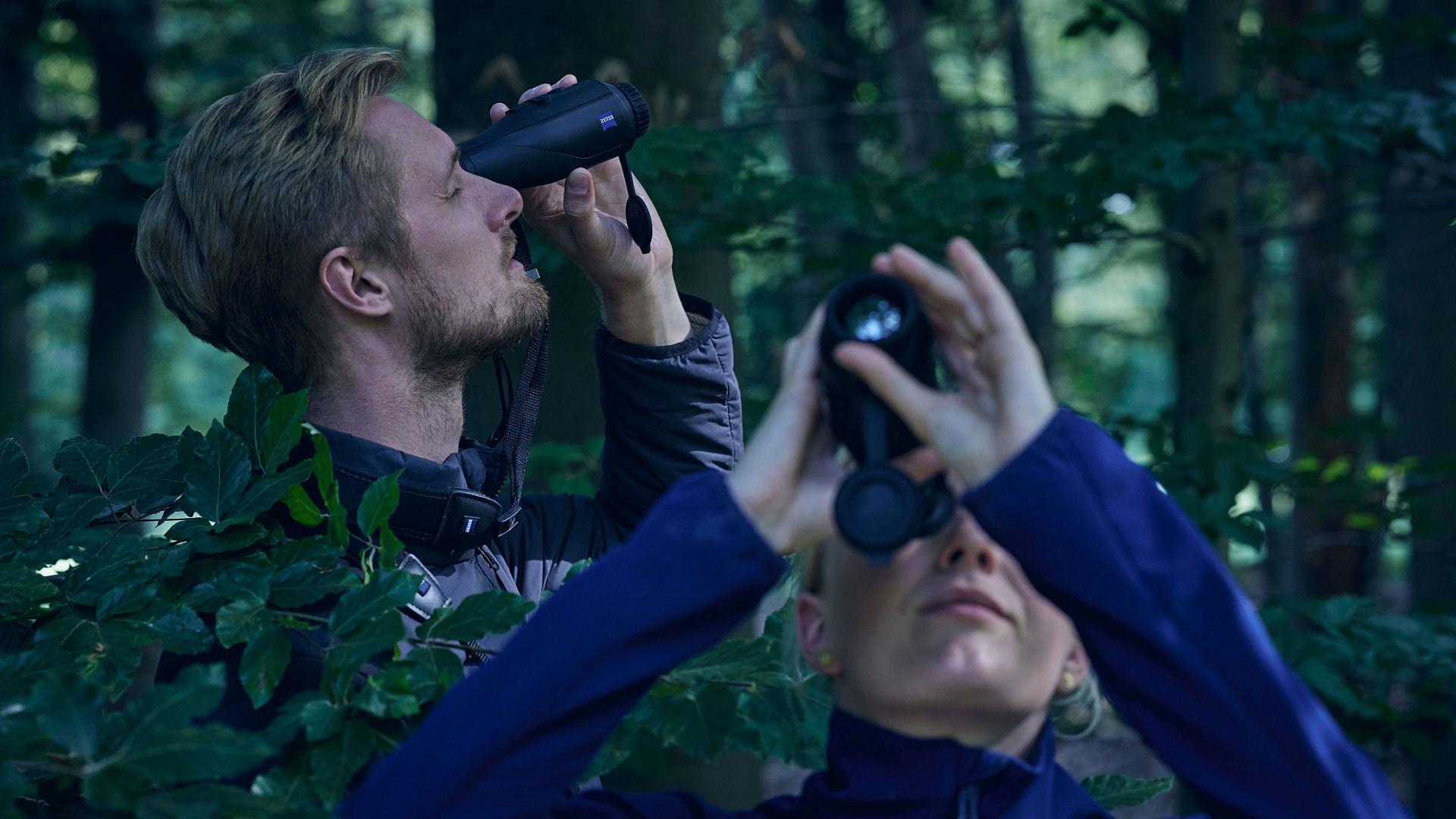 Two people in a forest are observing their surroundings using ZEISS optics.