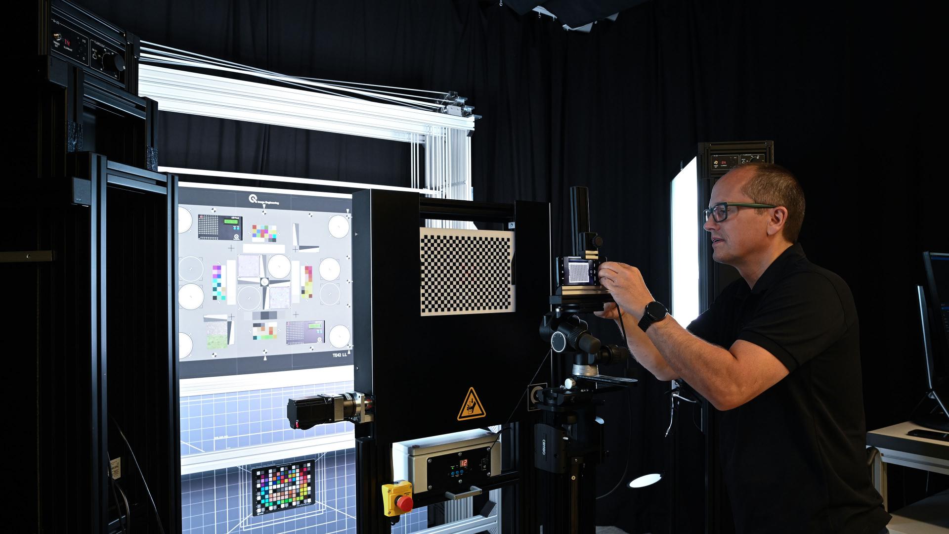 A ZEISS engineer adjusts a high-precision mobile imaging test setup in a controlled lab environment with calibration charts and advanced optical equipment.
