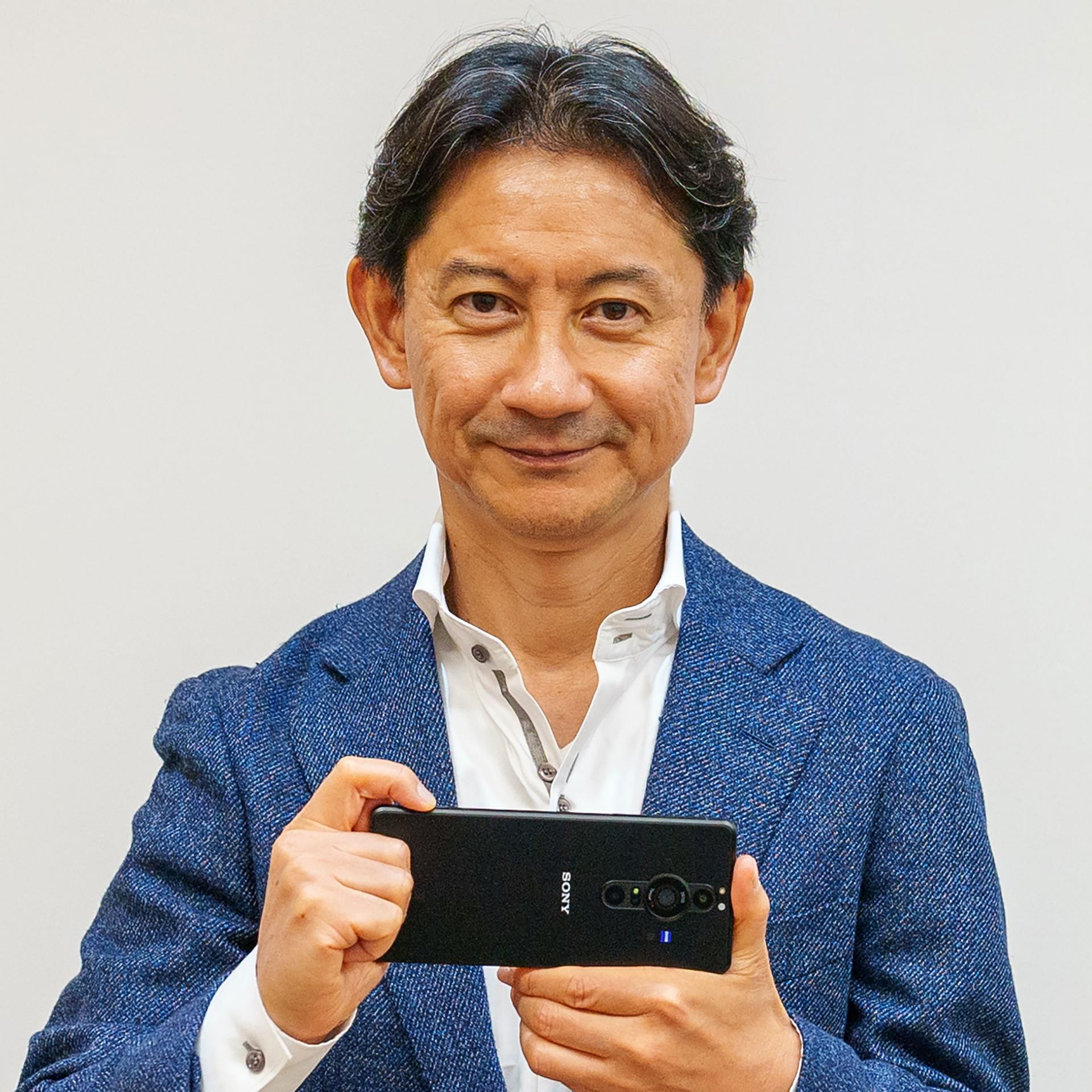 Man in a blue suit holding a smartphone with ZEISS optics in front of a wall with the SONY logo.
