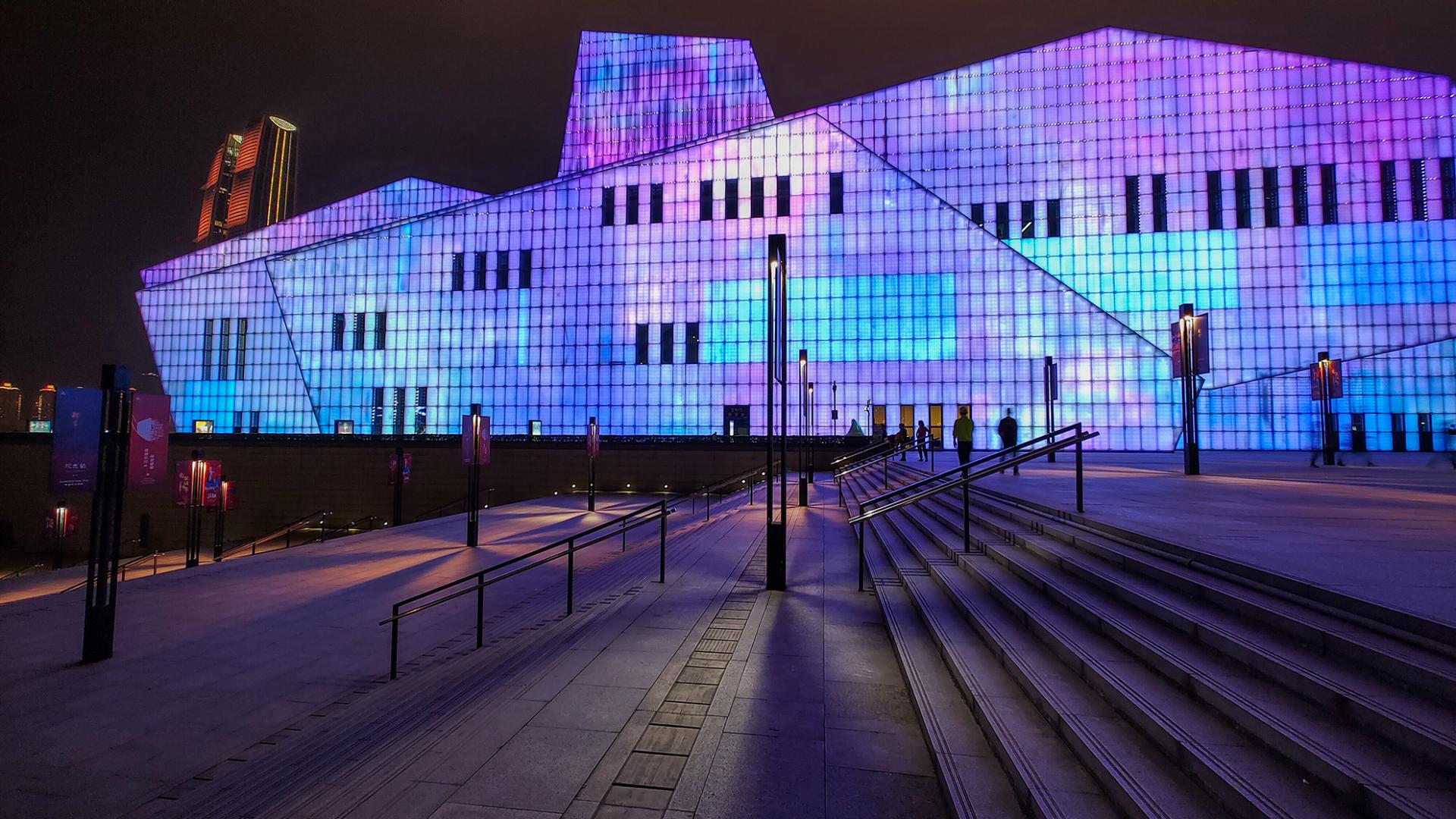 Modern building illuminated with vibrant purple and blue lights at night, with wide stone steps and handrails in the foreground.