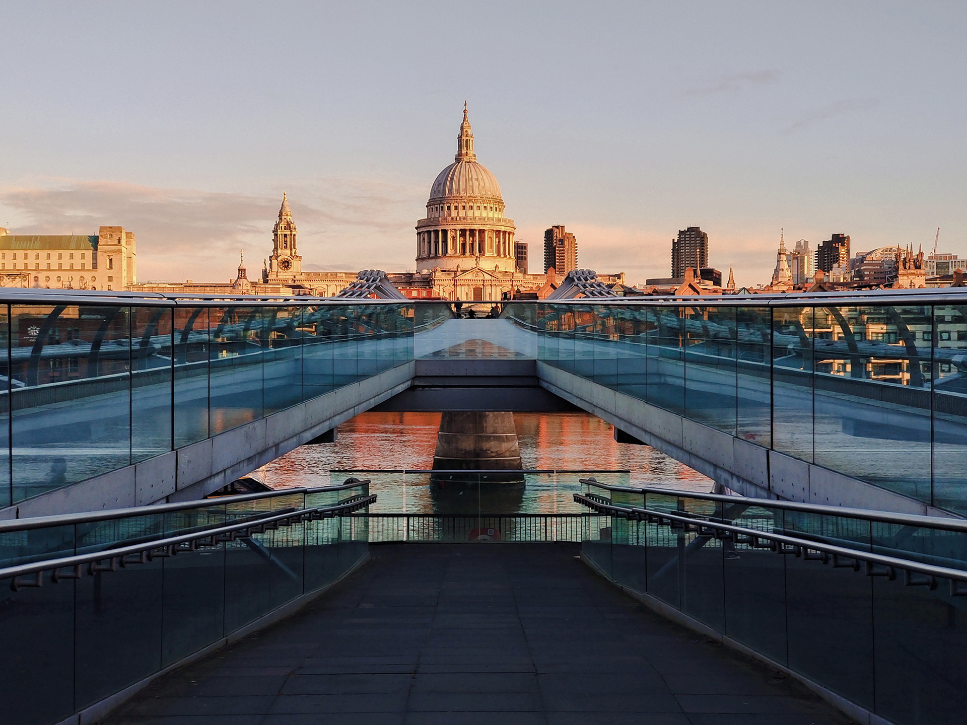 View of St. Paul’s Cathedral in London at sunset, seen from the Millennium Bridge with modern glass railings in the foreground.