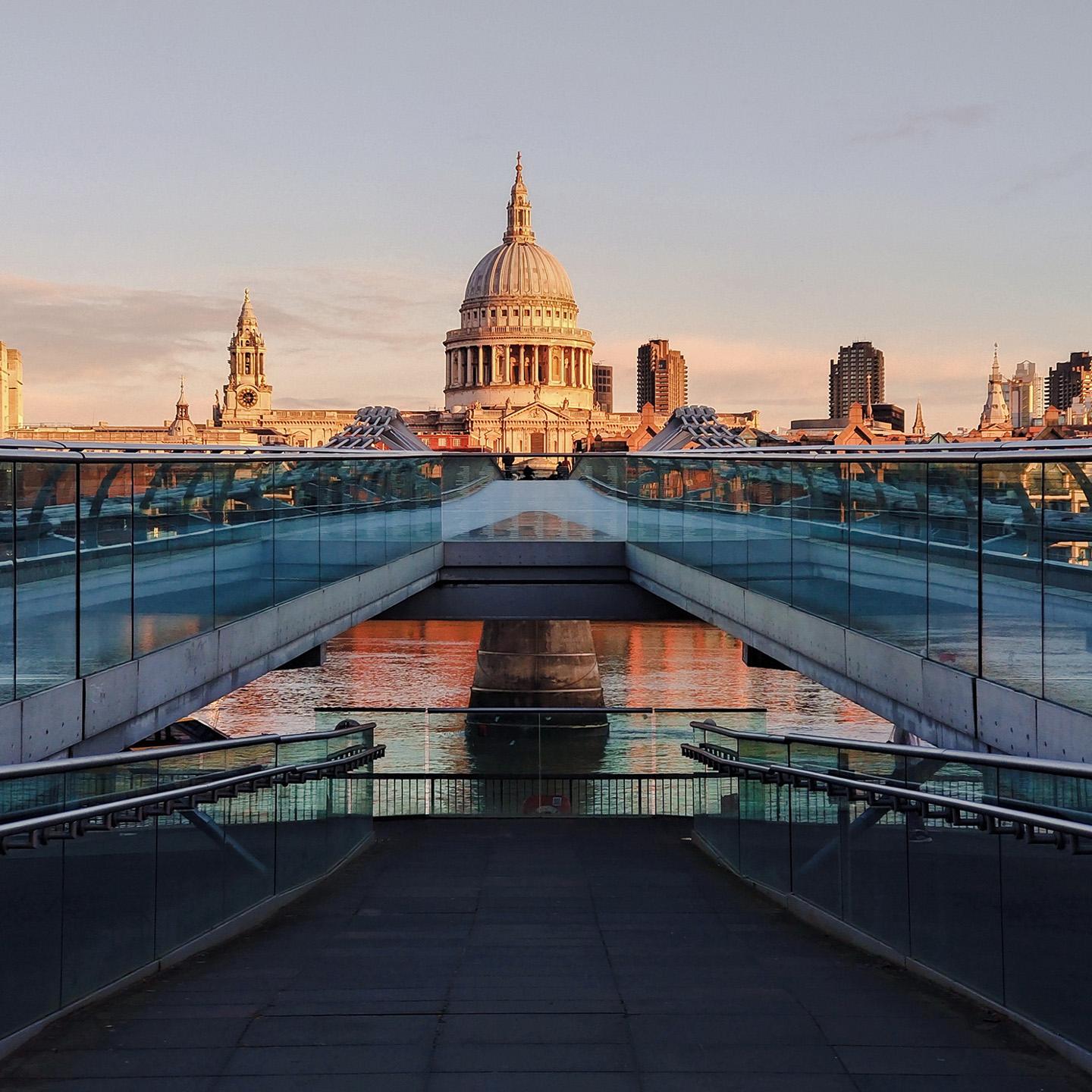 View of St. Paul’s Cathedral in London at sunset, seen from the Millennium Bridge with modern glass railings in the foreground.