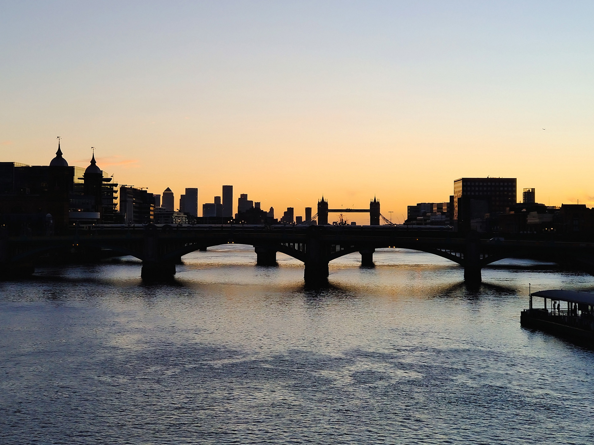 Silhouette of London's skyline and Tower Bridge at sunset, viewed across the River Thames.