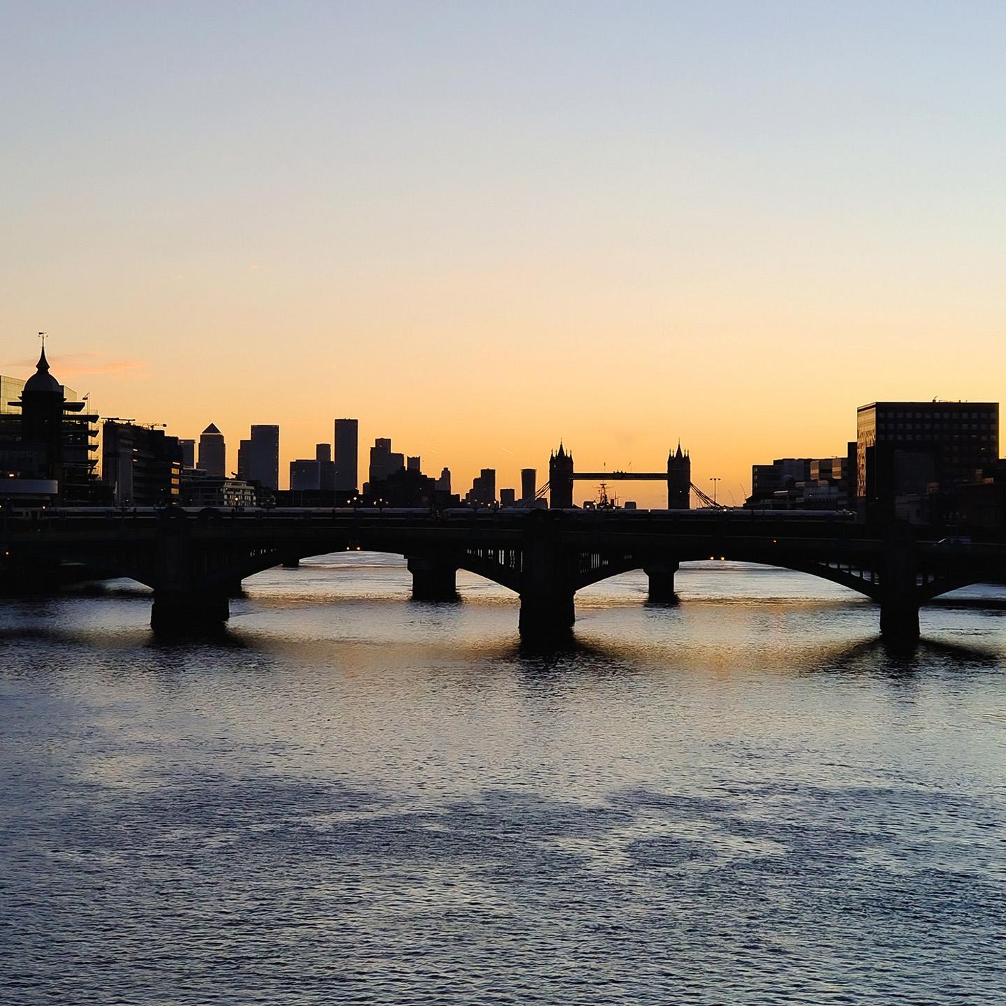 Silhouette of London's skyline and Tower Bridge at sunset, viewed across the River Thames.