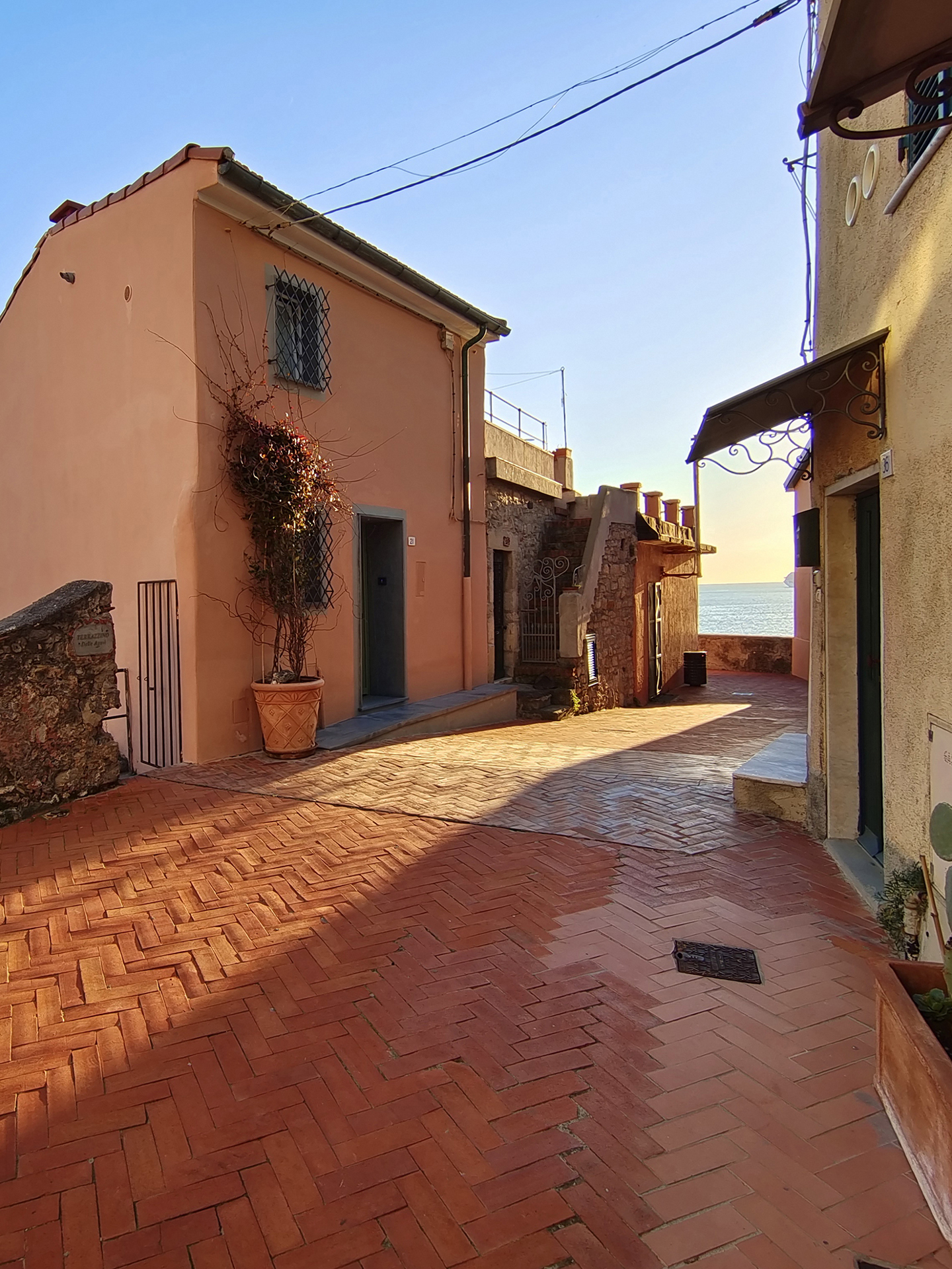 A sunlit cobblestone alley with pastel-colored buildings and a view of the sea in the distance, captured with sharp detail and vibrant colors, demonstrating ZEISS optical clarity.