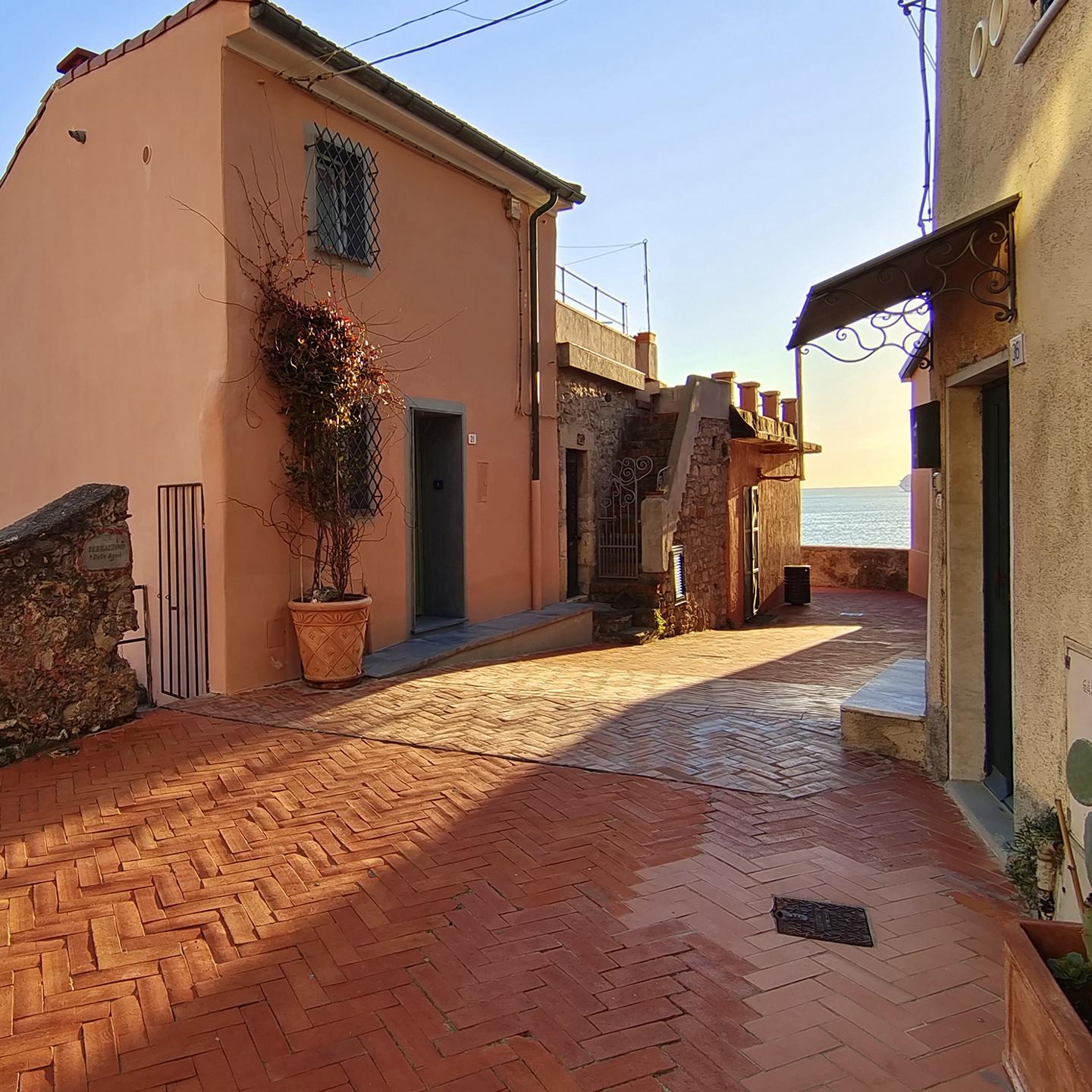 A sunlit cobblestone alley with pastel-colored buildings and a view of the sea in the distance, captured with sharp detail and vibrant colors, demonstrating ZEISS optical clarity.