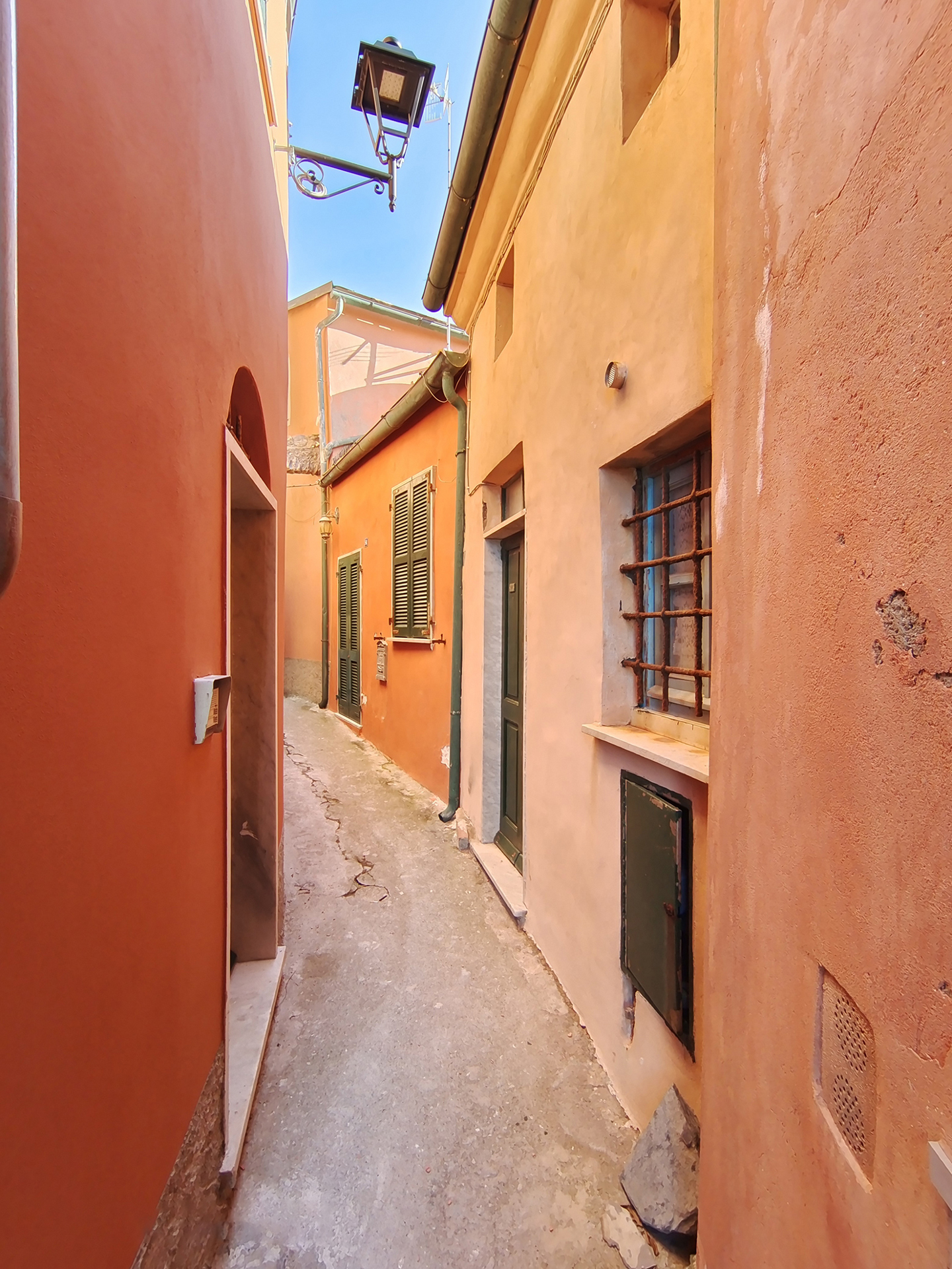 Narrow alleyway between colorful, sunlit buildings with textured walls and shuttered windows, captured in sharp detail with ZEISS optics.