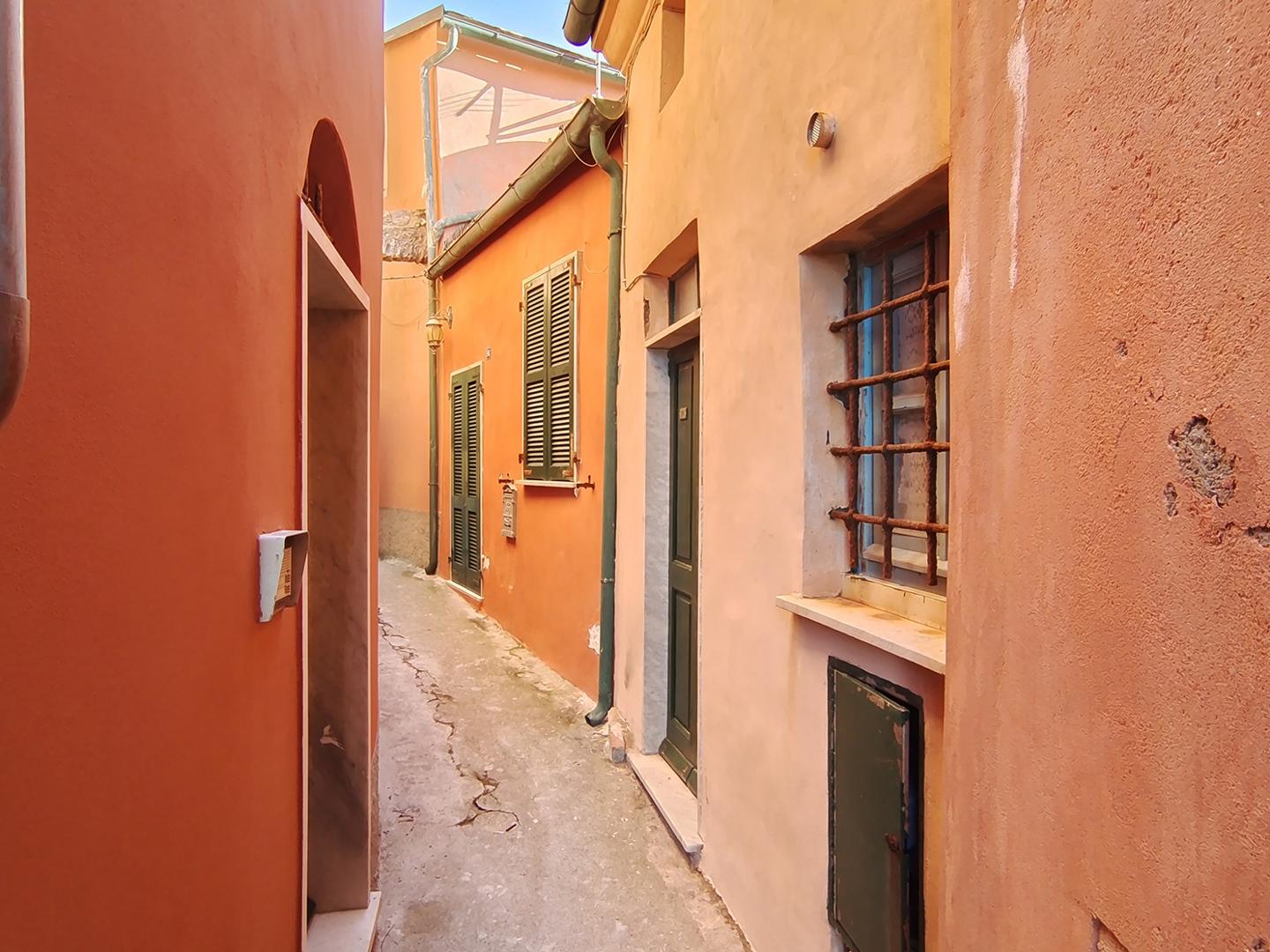 Narrow alleyway between colorful, sunlit buildings with textured walls and shuttered windows, captured in sharp detail with ZEISS optics.