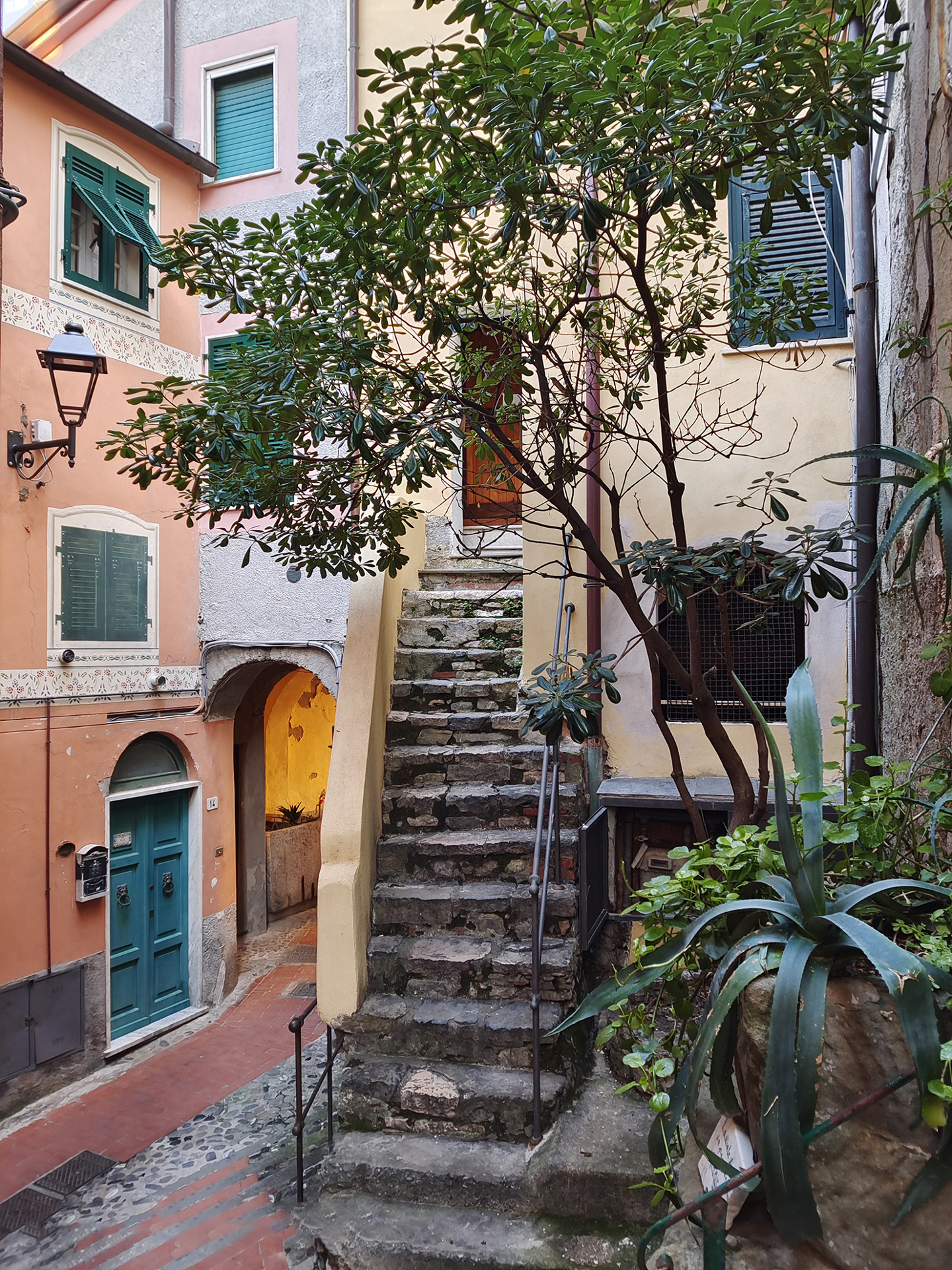 Stone staircase surrounded by colorful buildings and lush greenery in a quaint European alleyway, captured with crisp detail and vibrant colors by a ZEISS camera.