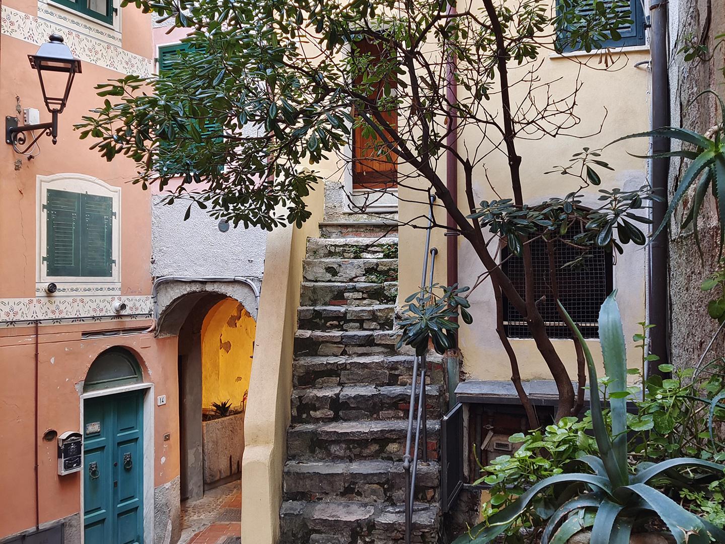 Stone staircase surrounded by colorful buildings and lush greenery in a quaint European alleyway, captured with crisp detail and vibrant colors by a ZEISS camera.
