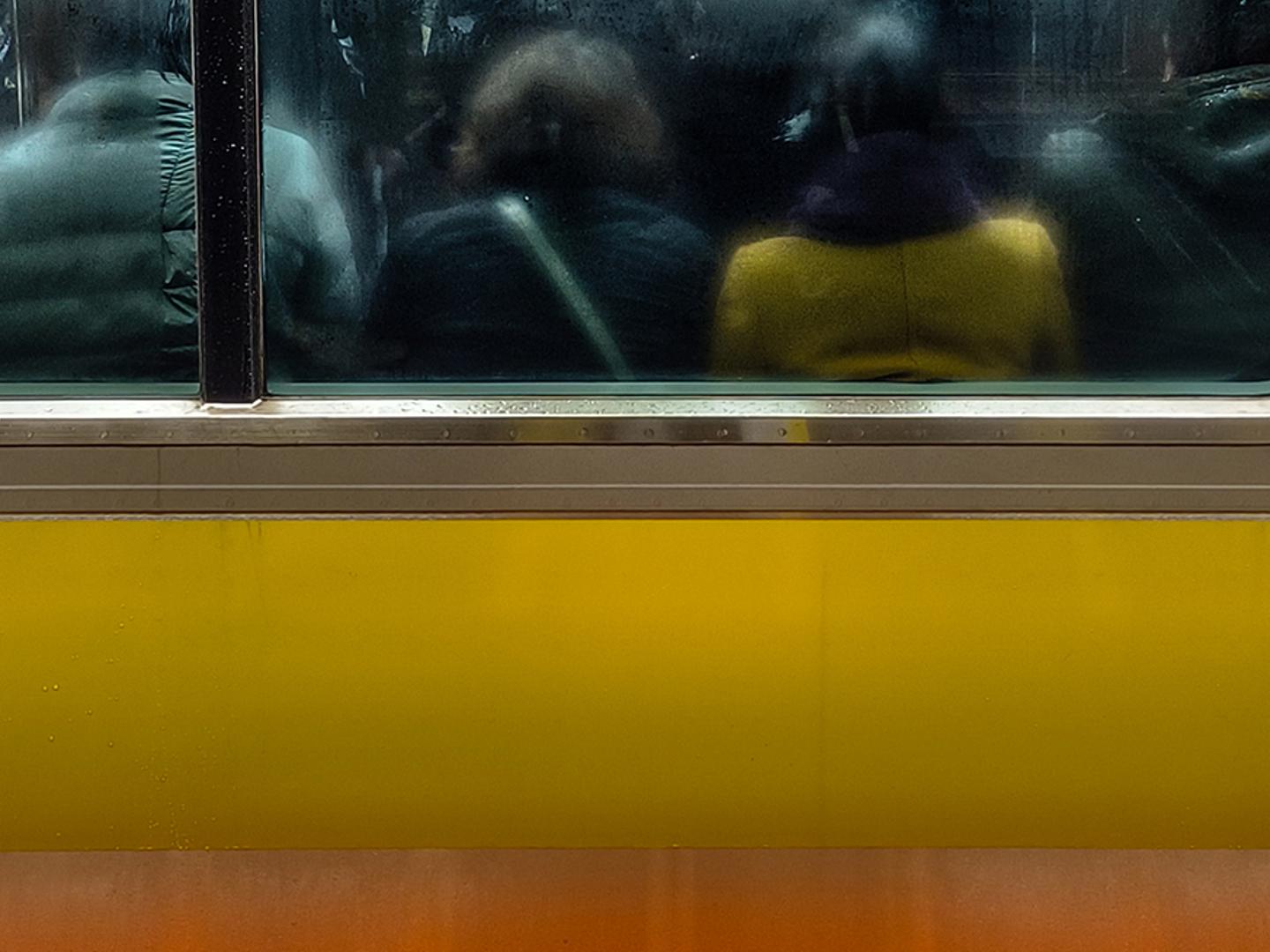 Passengers are seen through a fogged and reflective window of a yellow and orange subway train.