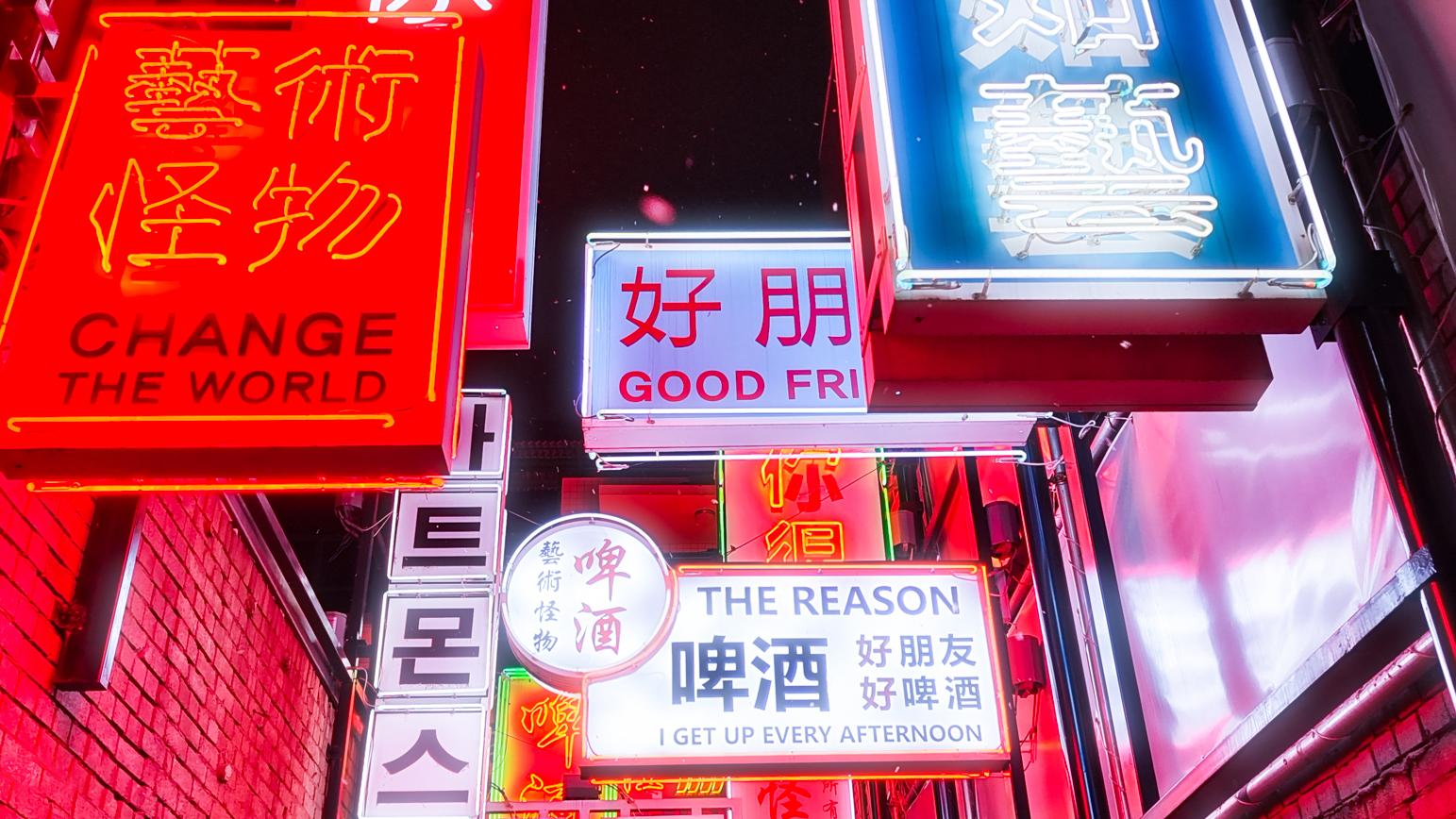 Colorful neon signs with various Chinese, Korean, and English text illuminate a narrow urban alleyway at night.