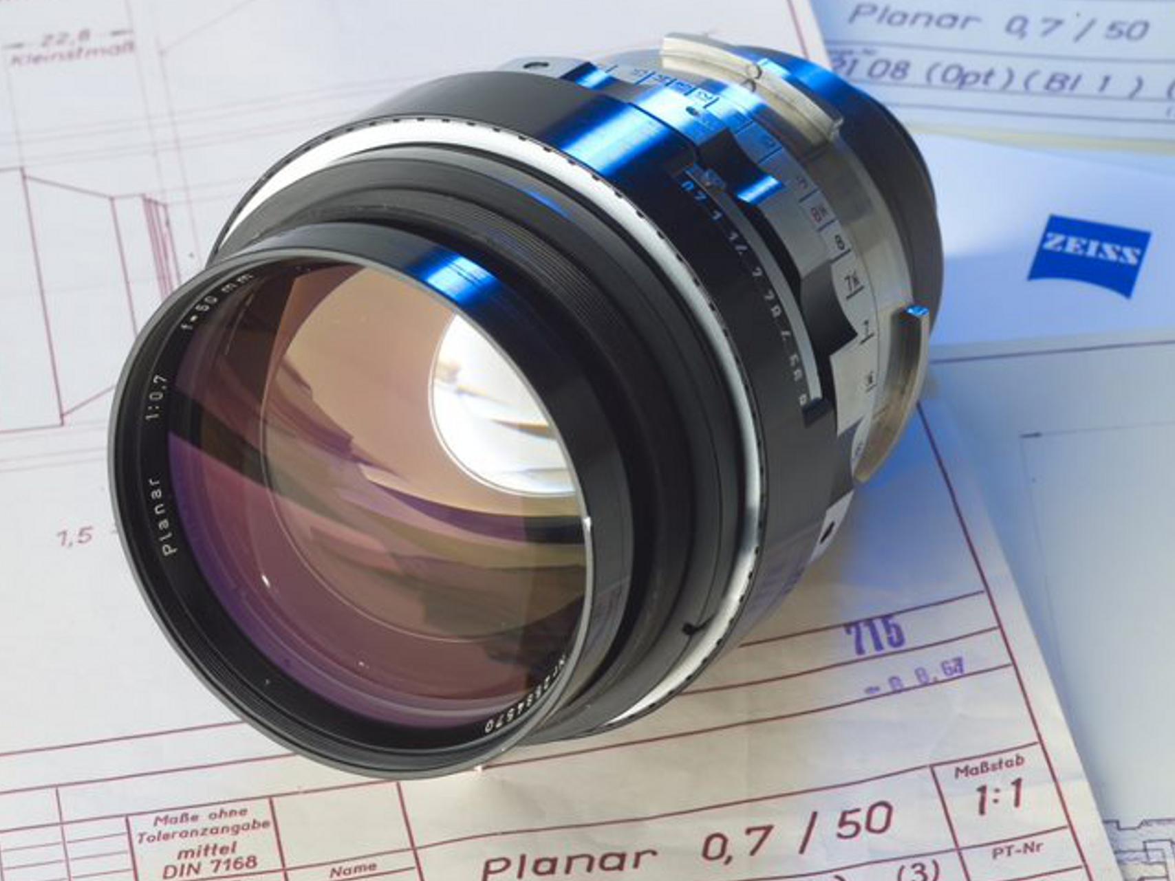 ZEISS camera lens placed on top of technical drawings and schematics related to the Planar 0.7/50 lens design.