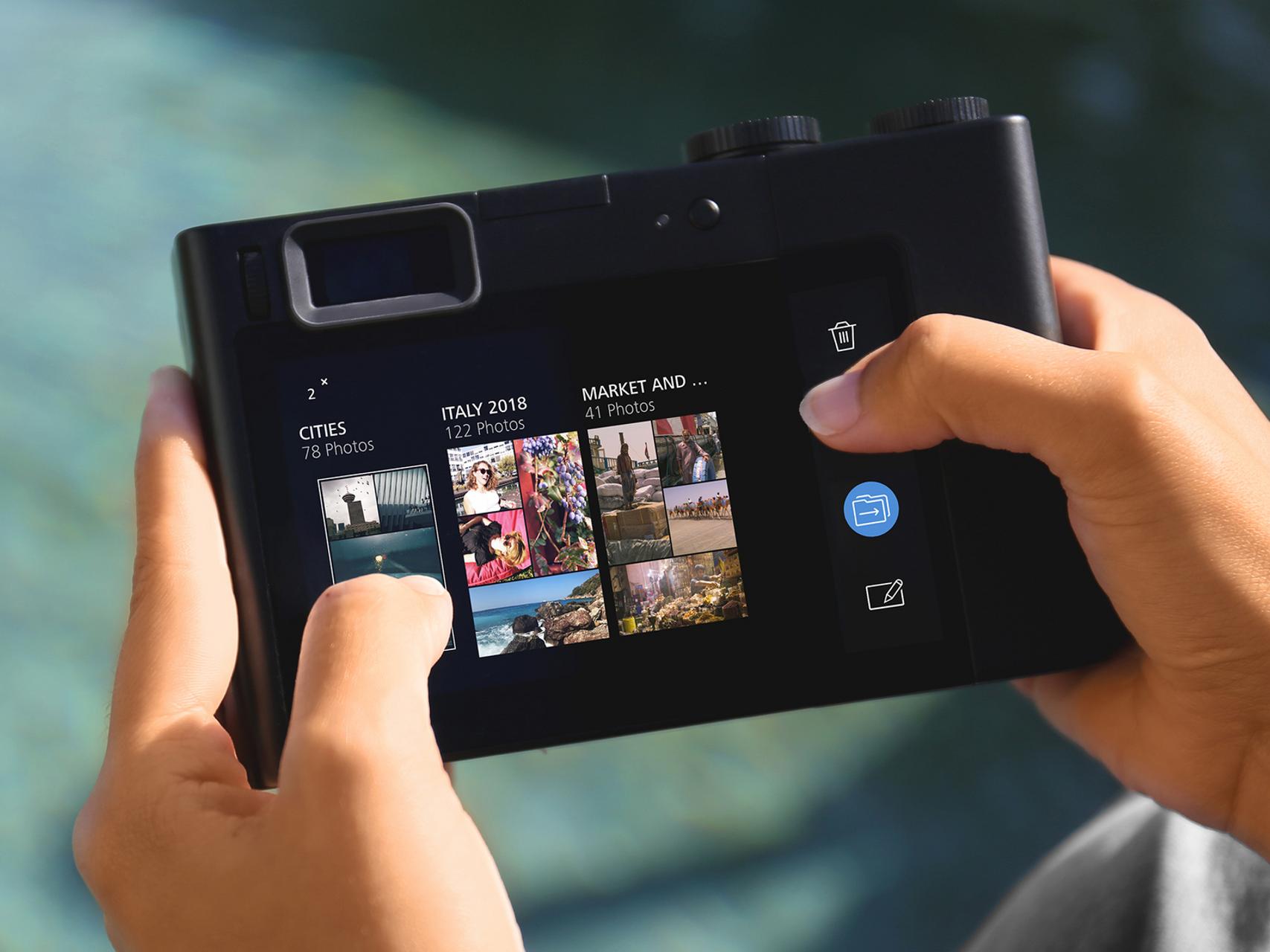 Hands holding a ZEISS camera with a touchscreen displaying photo albums and image thumbnails.