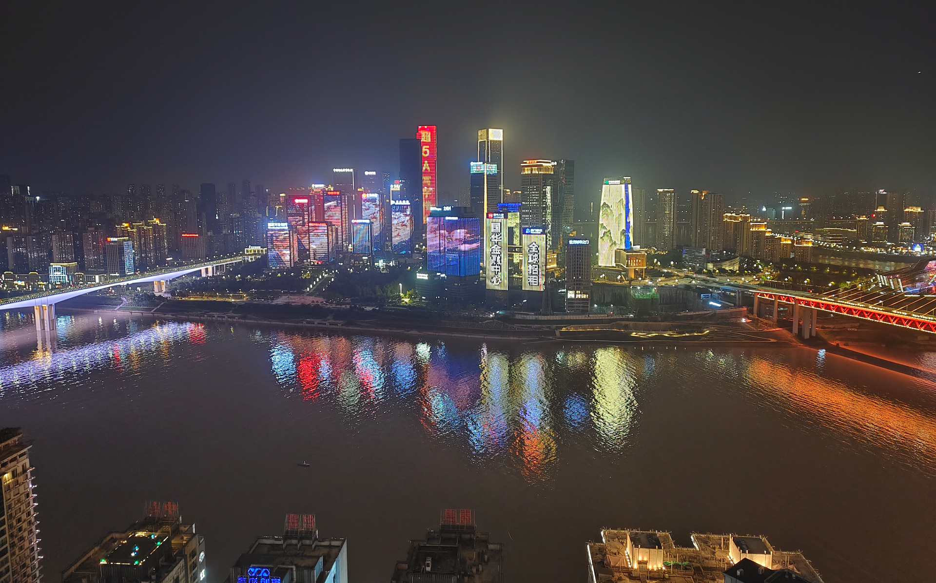 Nighttime cityscape with brightly illuminated skyscrapers reflecting in a wide river, showcasing the clarity and detail captured, ideal for ZEISS optical technology.