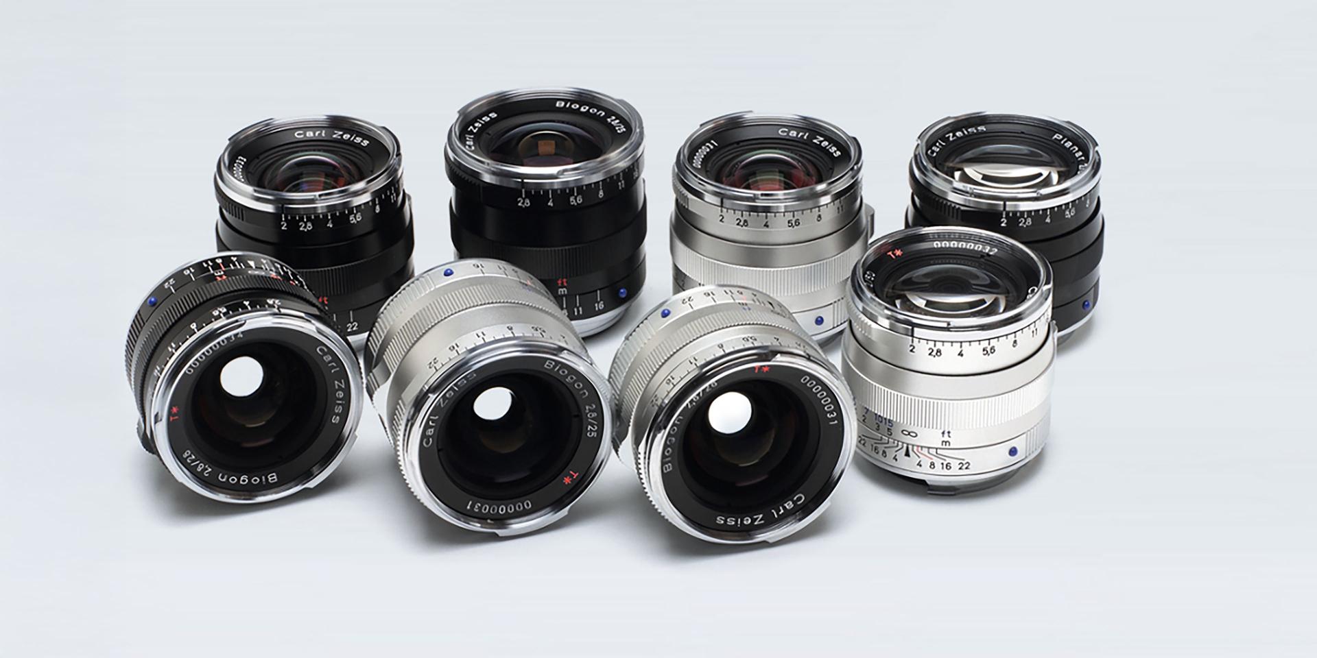 A collection of nine ZEISS camera lenses in black and silver finishes arranged on a light gray background.