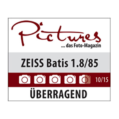 Review graphic from "Pictures – das Foto-Magazin" showing the ZEISS Batis 1.8/85 lens rated 10 out of 15 with the verdict "ÜBERRAGEND" (outstanding).