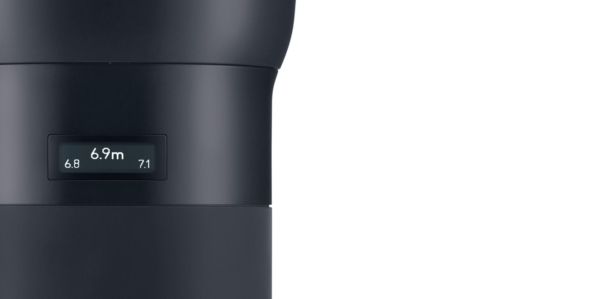 Close-up of a ZEISS camera lens displaying focus distance and aperture settings on a digital screen.