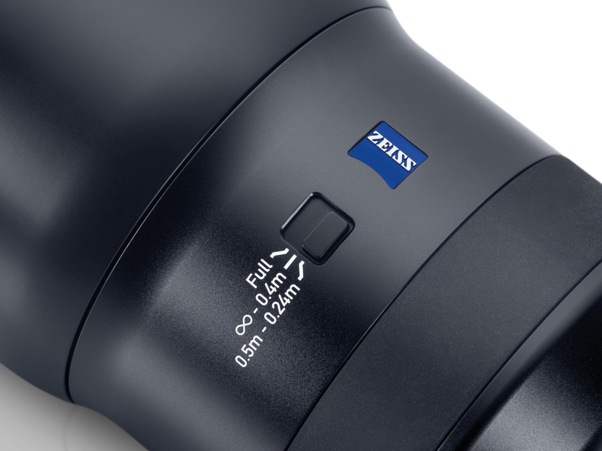 Close-up of a ZEISS camera lens showing a focus range switch with distance settings and the ZEISS logo.