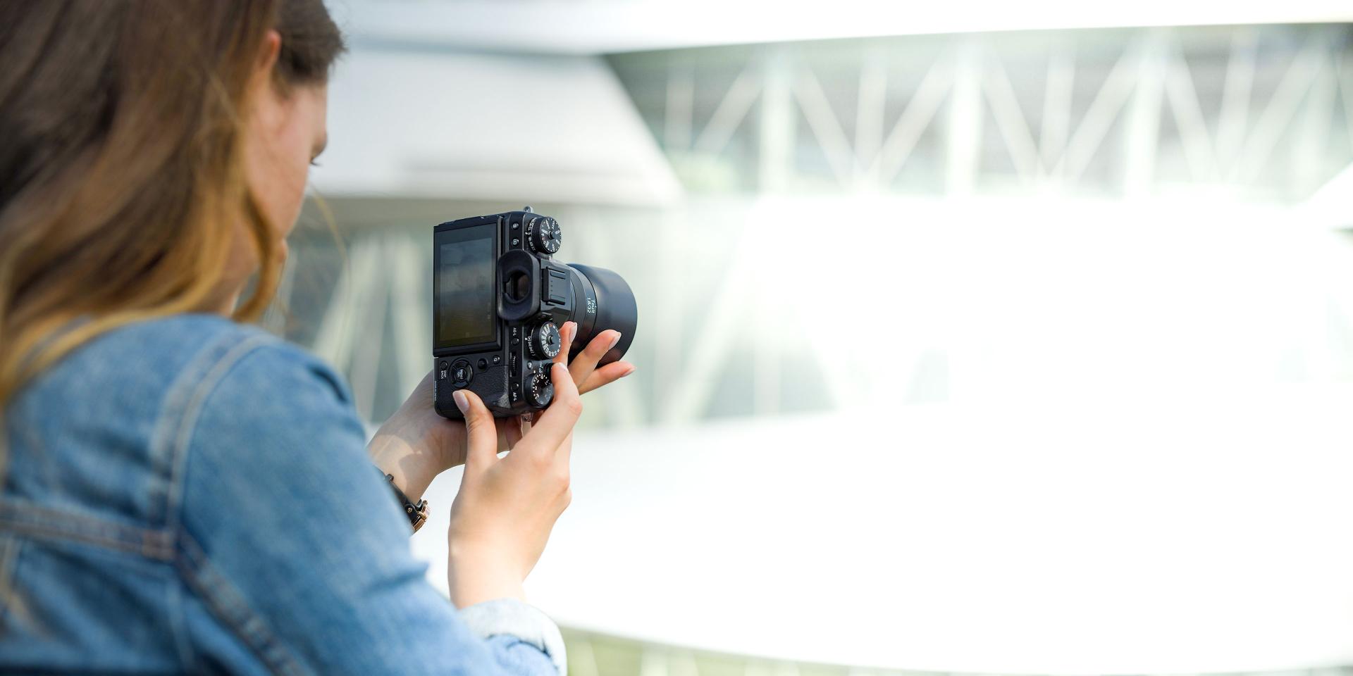 Person holding a professional camera equipped with a ZEISS lens in an outdoor setting.