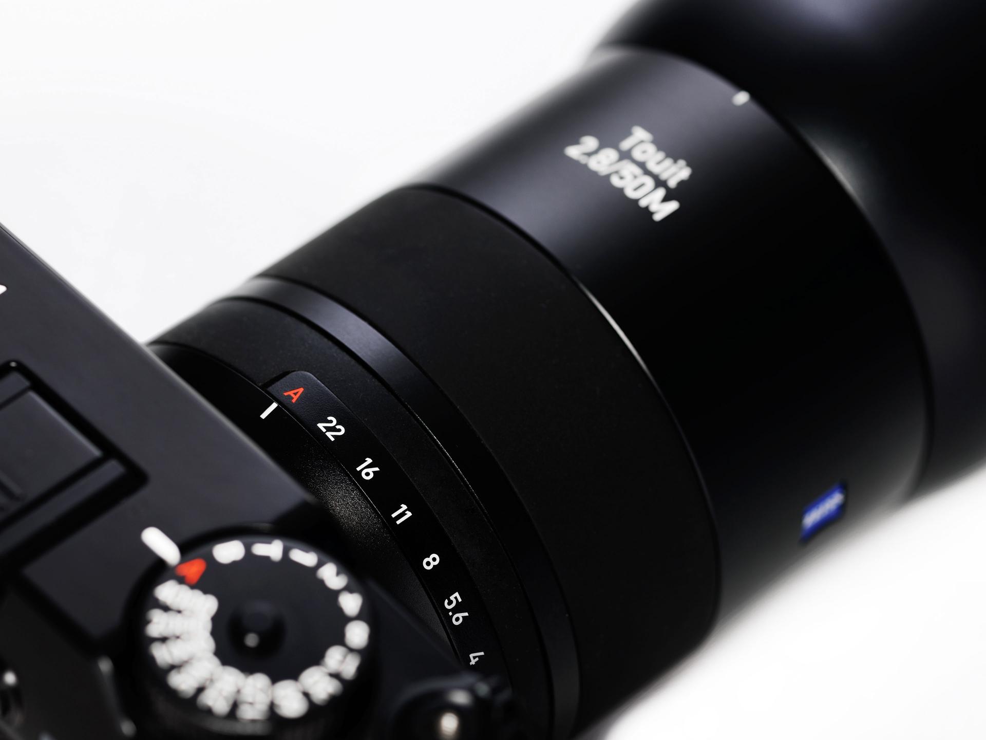 Close-up view of a ZEISS Touit 2.8/50M camera lens showing the front glass element and branding.