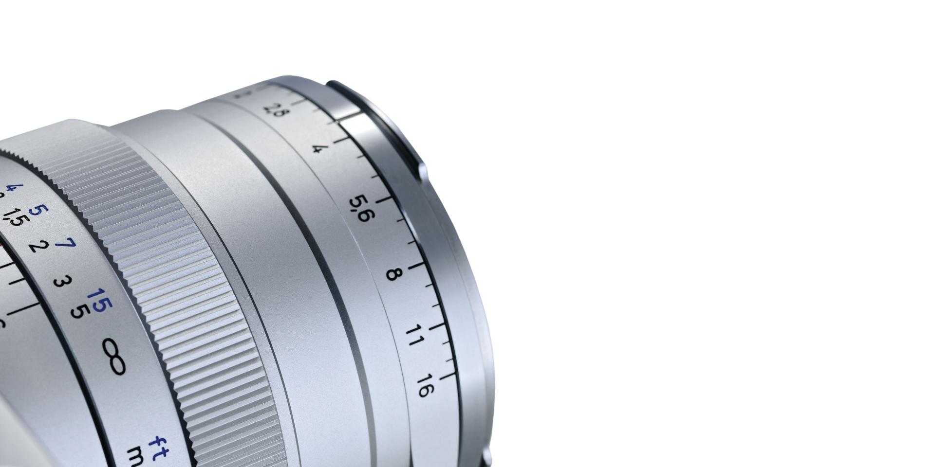 Close-up of a silver ZEISS camera lens showing focus and aperture markings.