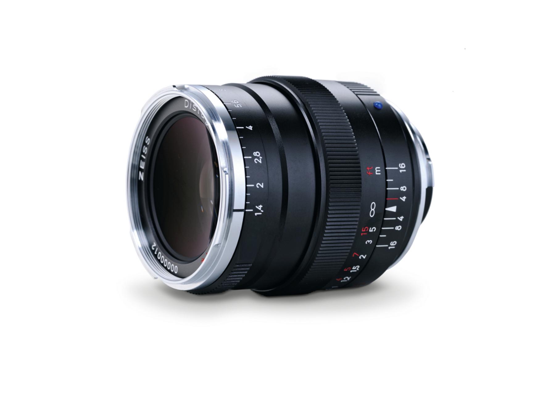 A black ZEISS camera lens with manual focus and aperture rings is displayed against a white background.