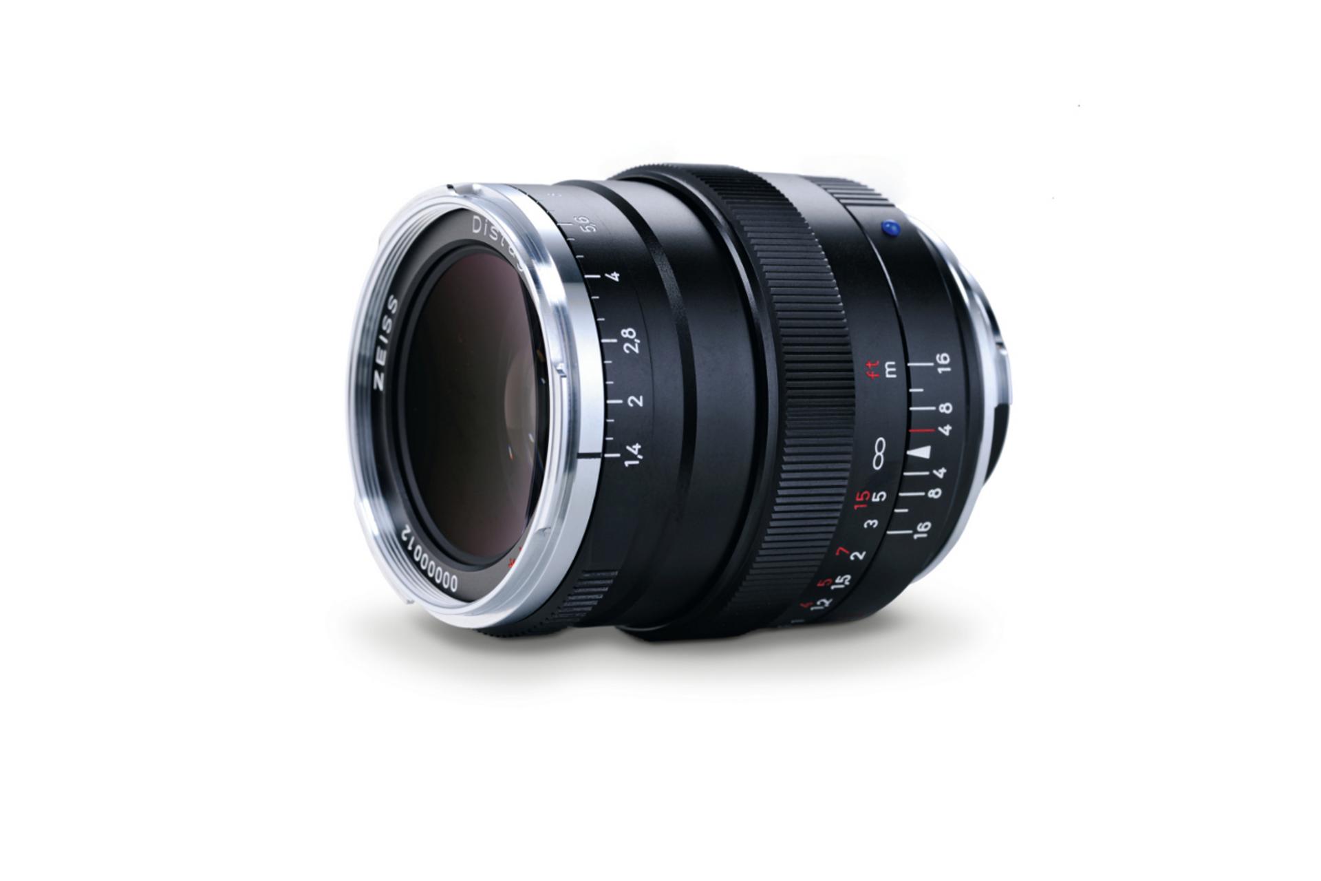 A black ZEISS camera lens with manual focus and aperture rings is displayed against a white background.