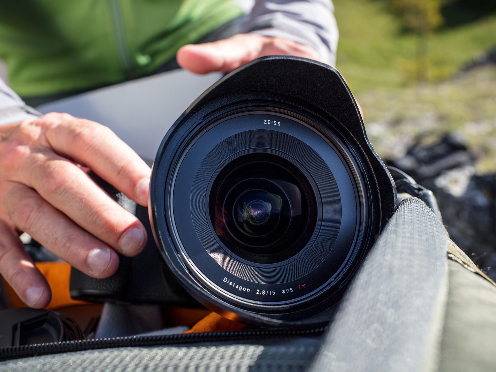 Close-up of a ZEISS Distagon 2.8/15 camera lens being handled and placed into a padded camera bag outdoors.