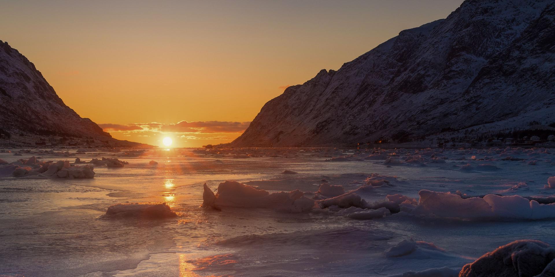 Frozen arctic landscape with icy water and snow-covered mountains under a warm sunset, showcasing ZEISS lens clarity.