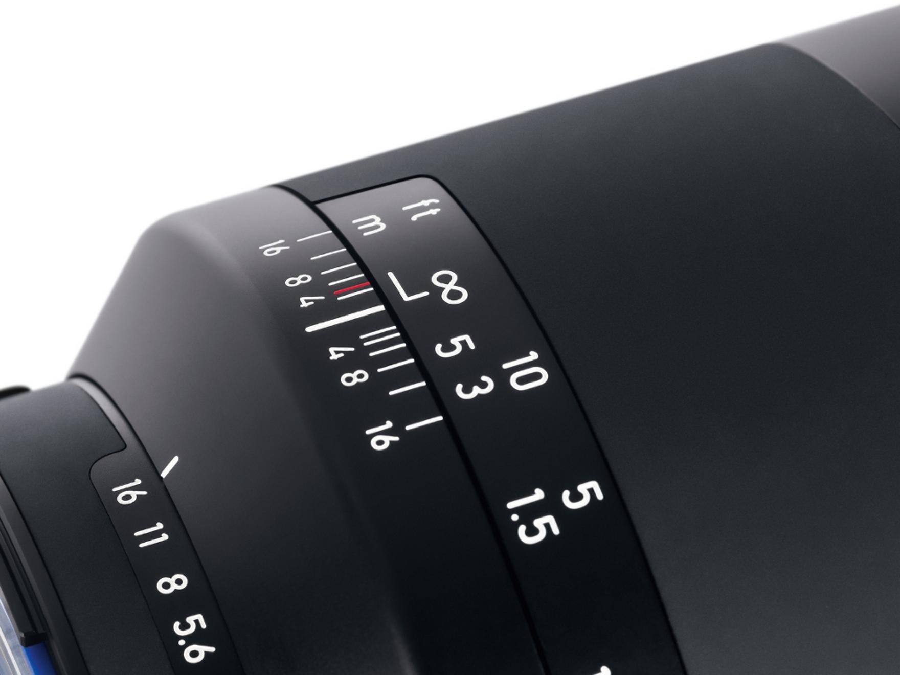 Close-up view of a ZEISS camera lens showing focus and aperture distance markings in feet and meters.