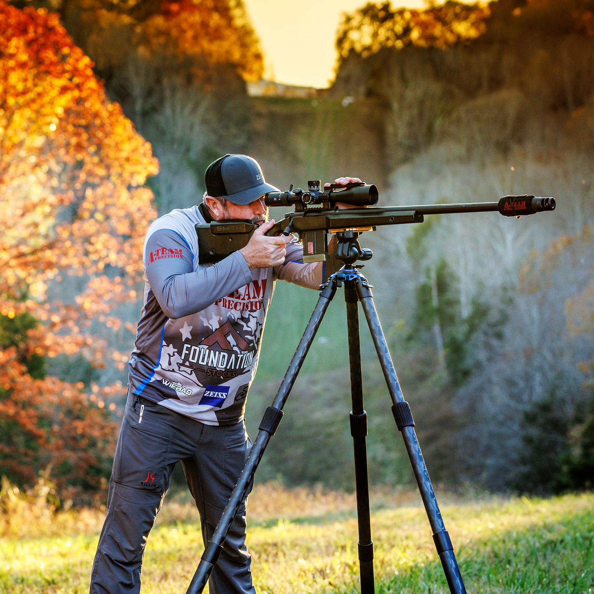 Two men using ZEISS optics mounted on tripods for spotting and precision shooting in a scenic outdoor setting with autumn foliage.