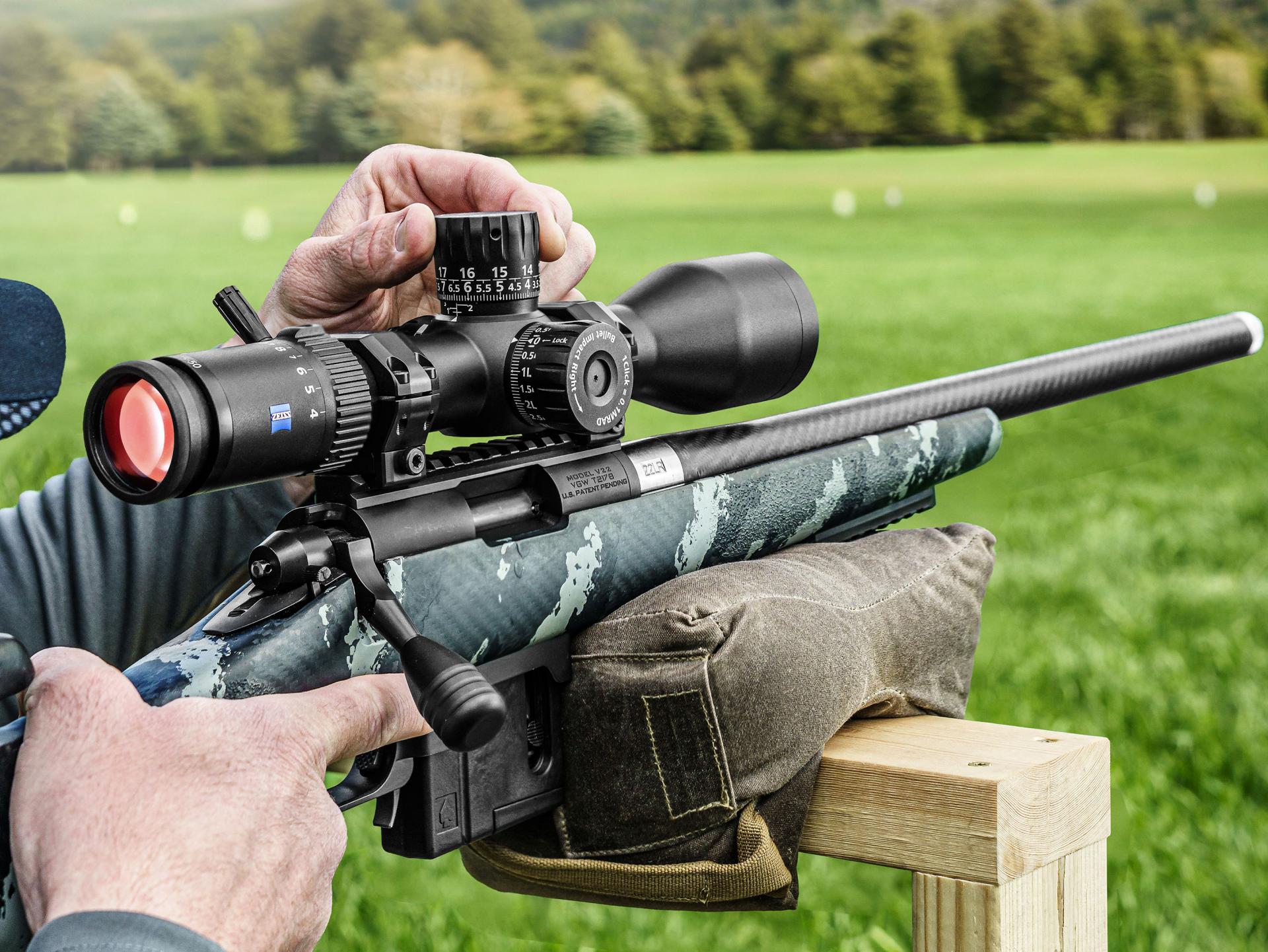 Person aiming a rifle equipped with a ZEISS riflescope at an outdoor shooting range.