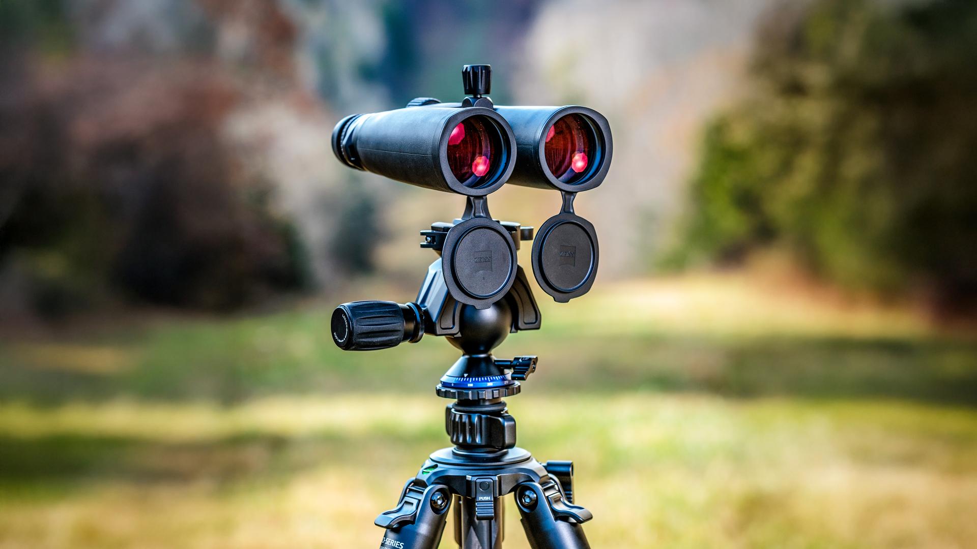 High-quality ZEISS binoculars mounted on a tripod, positioned outdoors with a blurred natural background.