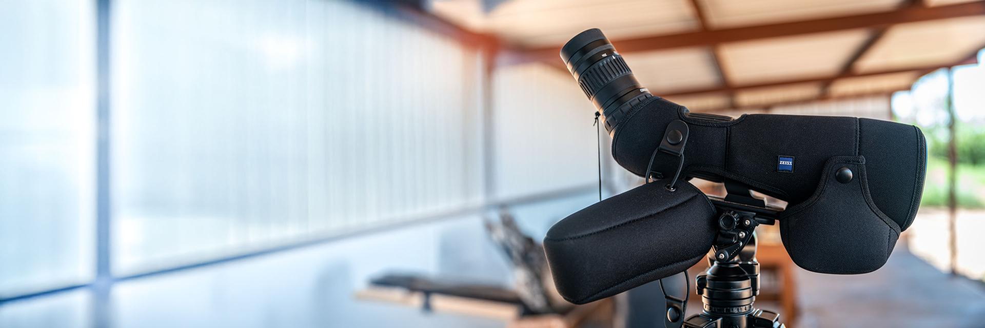 A ZEISS spotting scope mounted on a tripod, covered with a protective black case featuring the ZEISS logo.