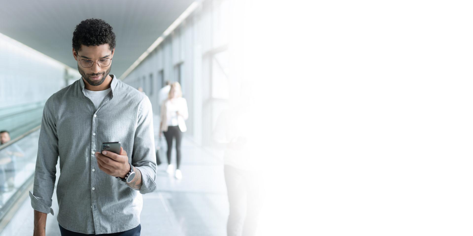 Young man wearing ZEISS SmartLife lenses looking at his phone while walking.