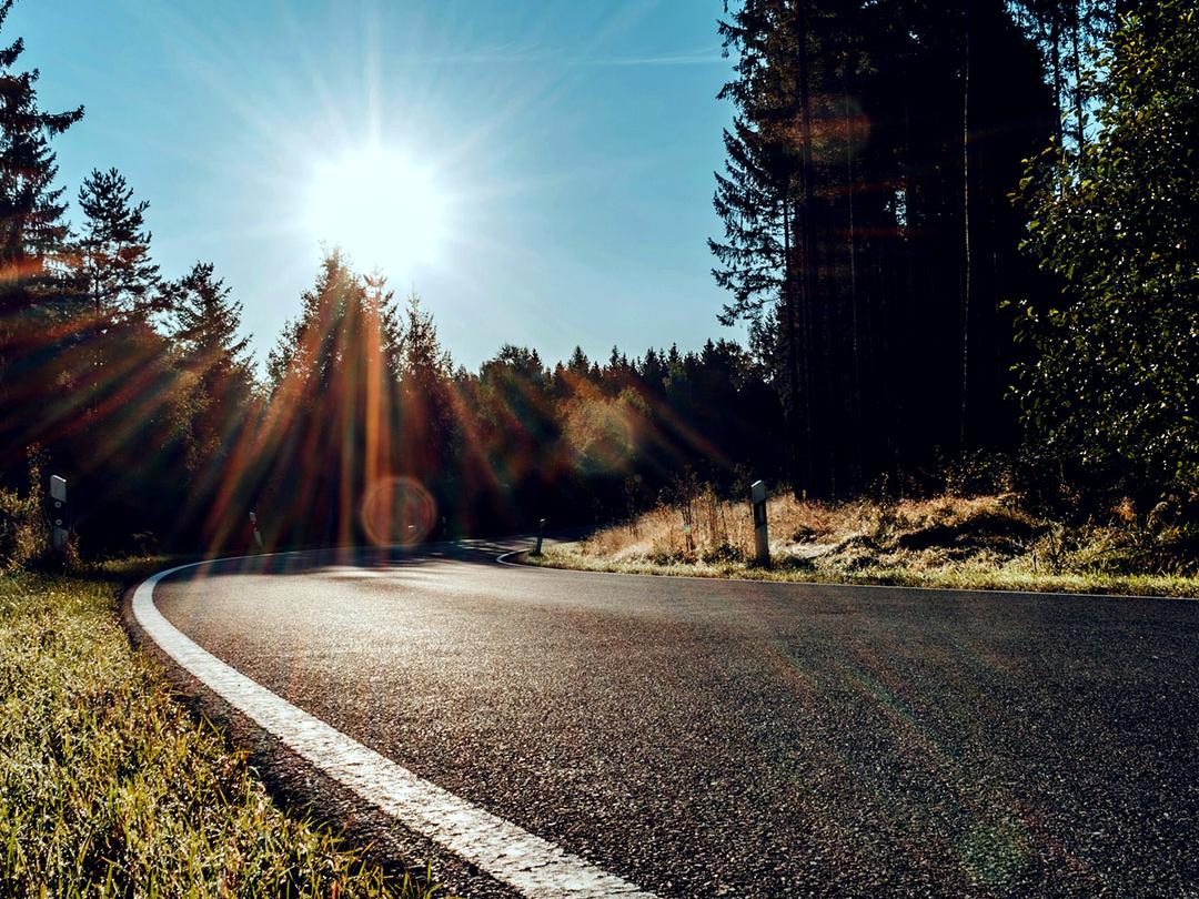 A slider image where one half shows a road in the woods with bright light from a sun, and the other half showing the same road with reduced glare and increased contrast, emphasising the effect of polarised sunglass lenses.