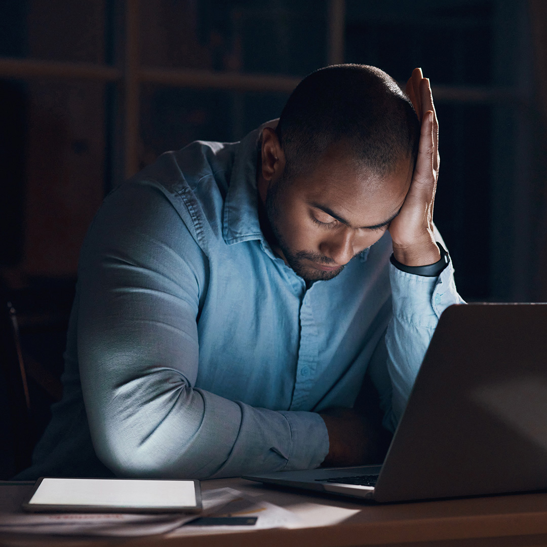 An image of a man in front of a computer screen holding his head.
