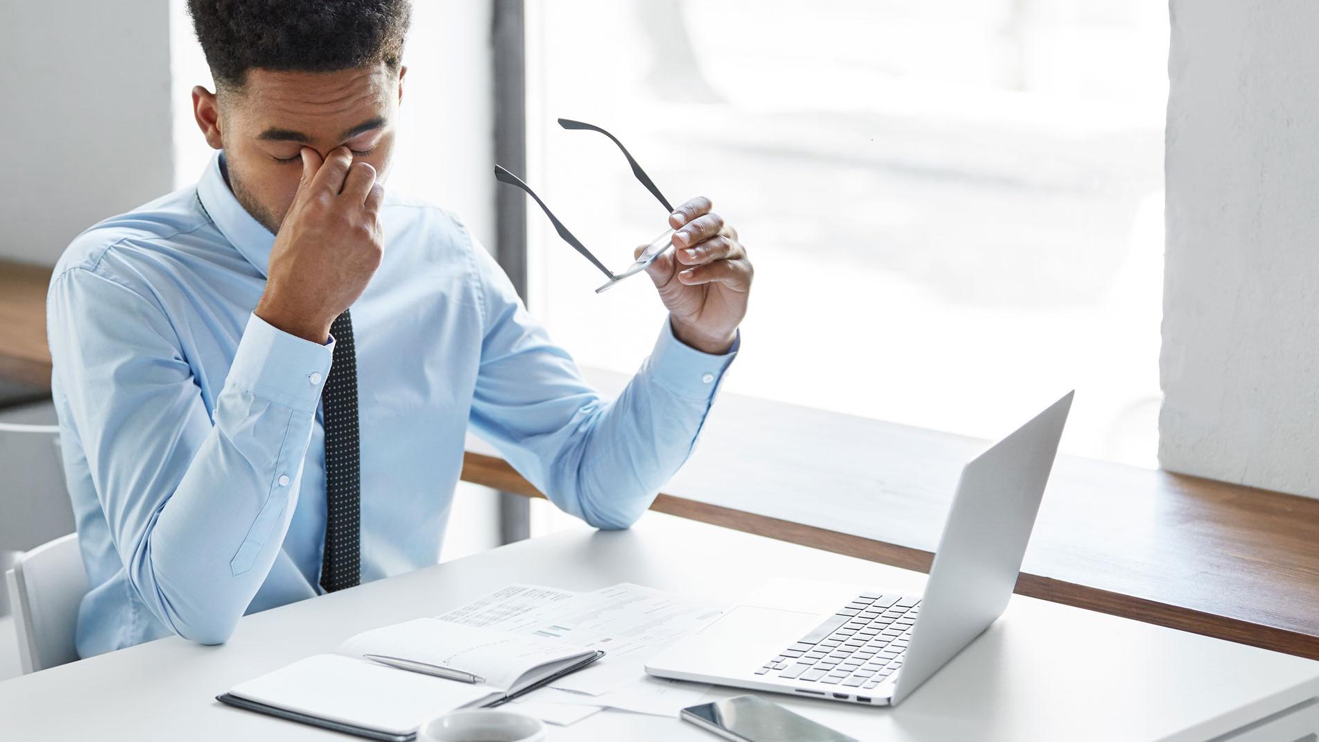 A man sits in front of laptop and is rubbing his eyes