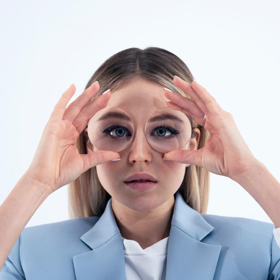 A young women holding two thick lenses in front of her eyes to show the fish bowl effect.