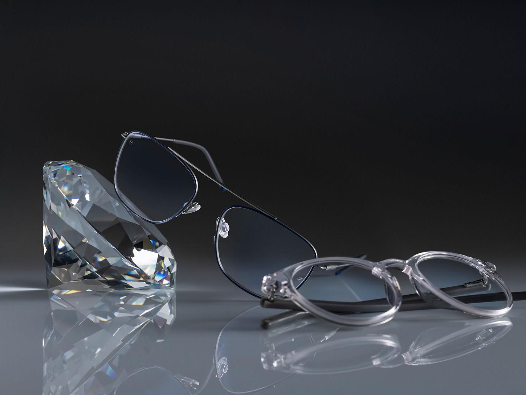 Two pairs of glasses with ZEISS lenses that have the hardest ZEISS coating ever - DuraVision® Platinum. One pair of glasses leans against a crystal, the other lies flat on the ground. Both feature clear lenses with no bluish reflection.