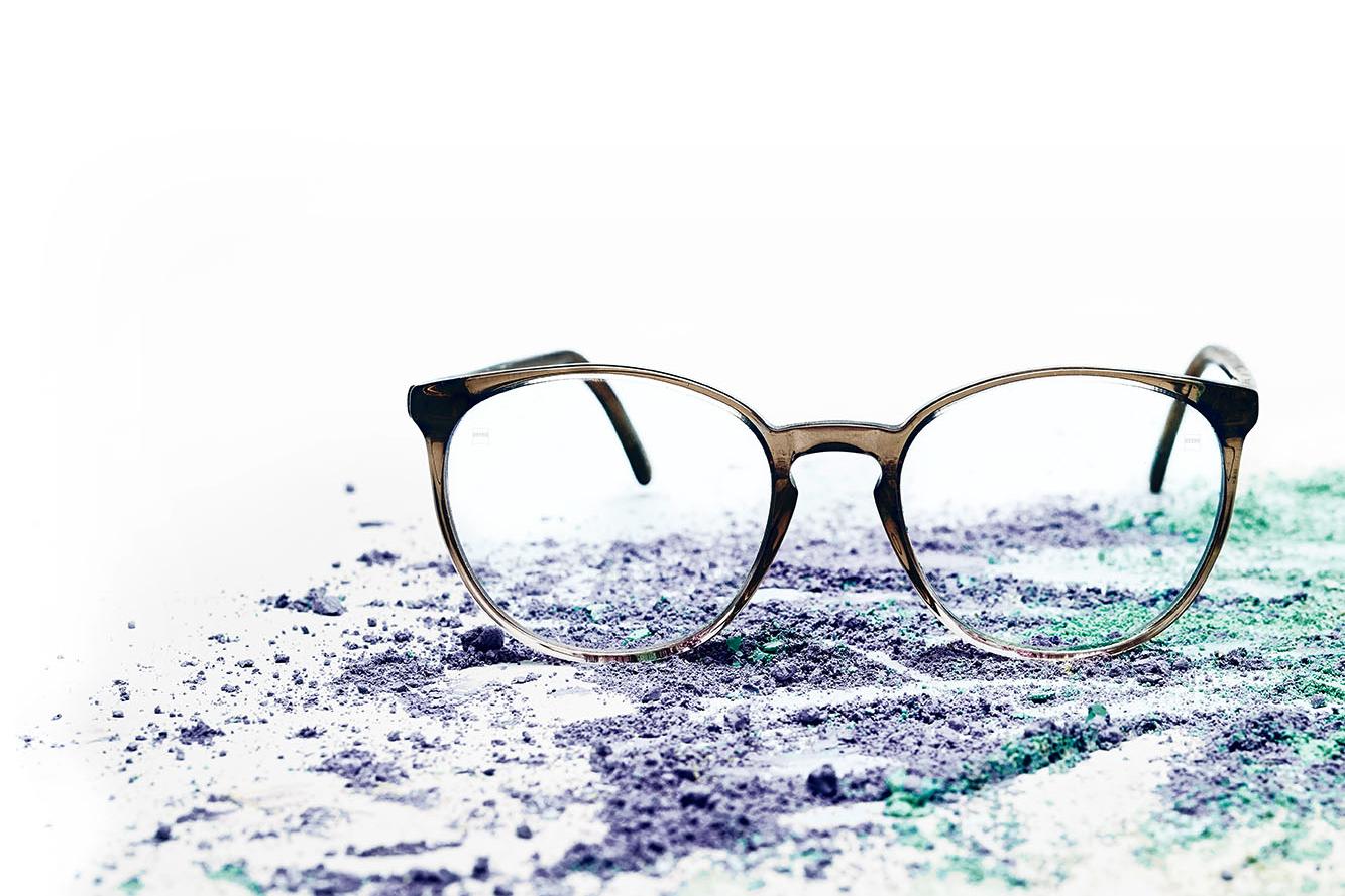 A pair of glasses with clear lenses lies on colorful powder.