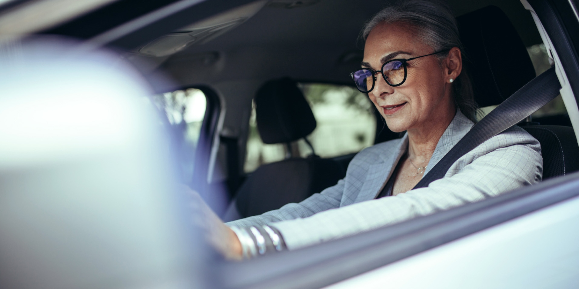A mature women in a car is wearing glasses with ZEISS DriveSafe lenses.